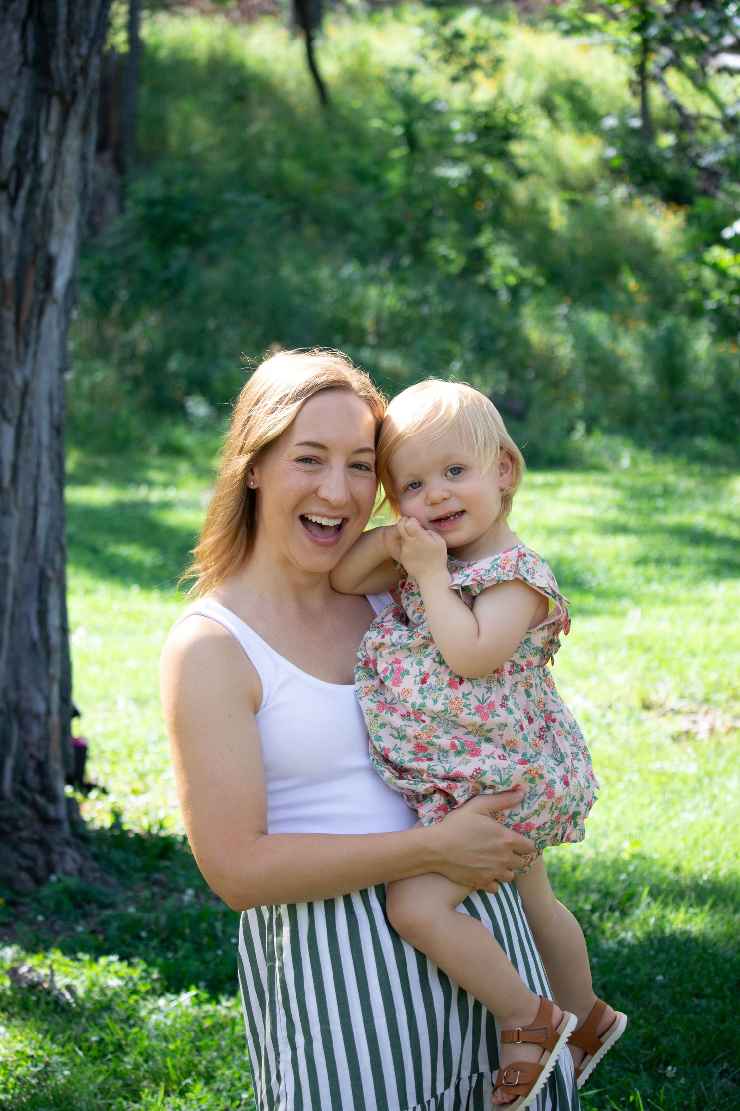 A joyful outdoor summer portrait showing shared laughter and hugs against a green natural backdrop in a park.