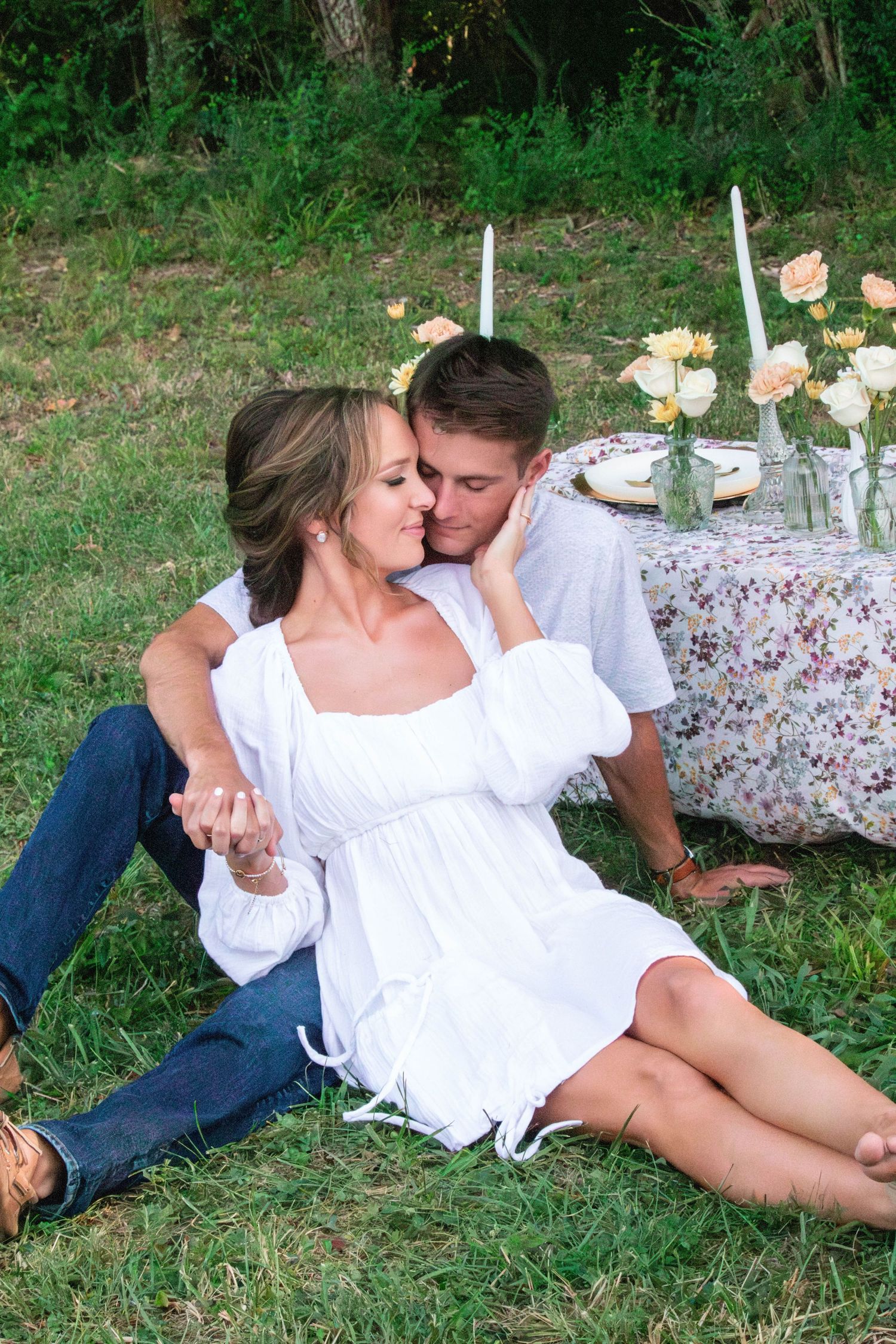 Romantic picnic scene on grass with floral tablecloth, candles and roses in a garden setting.