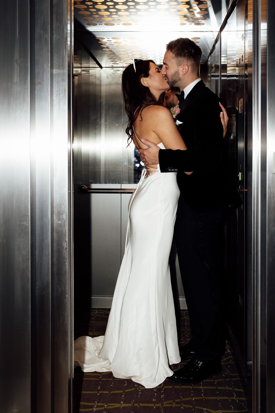 A couple shares an intimate moment in a candlelit elevator, with the bride wearing an elegant white fitted gown.