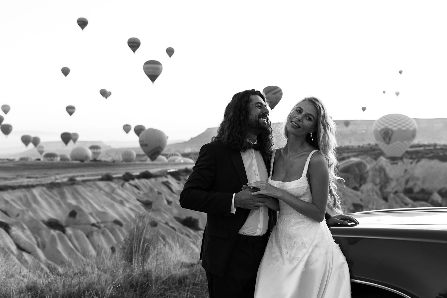 A couple embraces in front of hot air balloons floating over Cappadocia, Turkey in black and white.