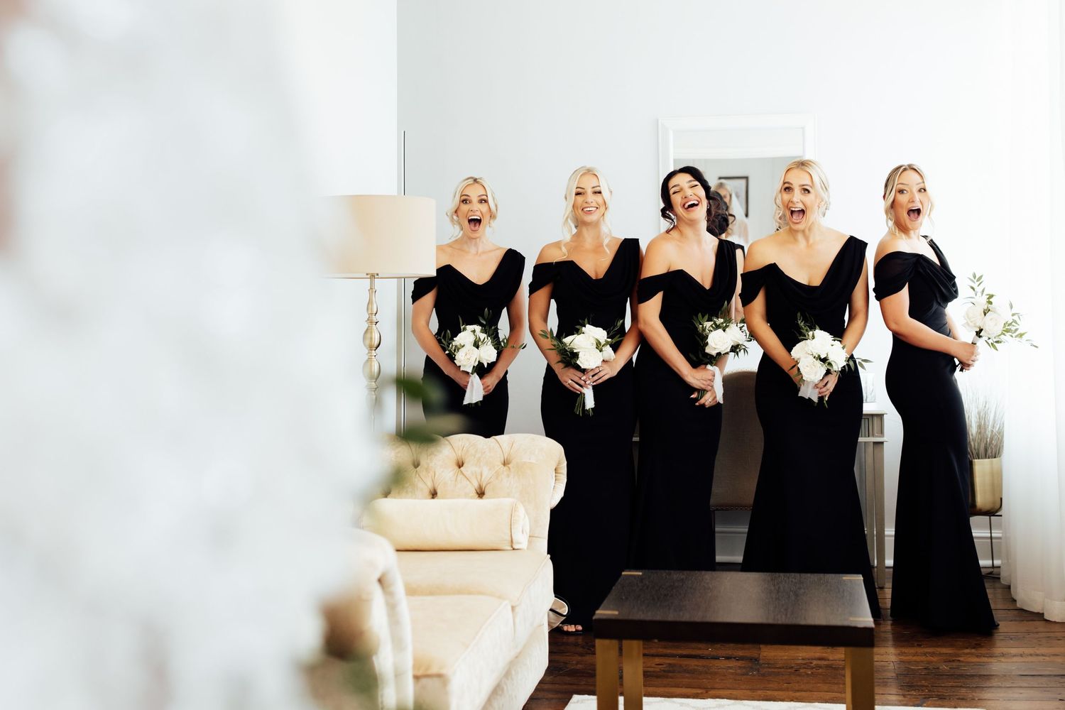 Bridesmaids in matching black dresses pose together for wedding photos in an elegant room.