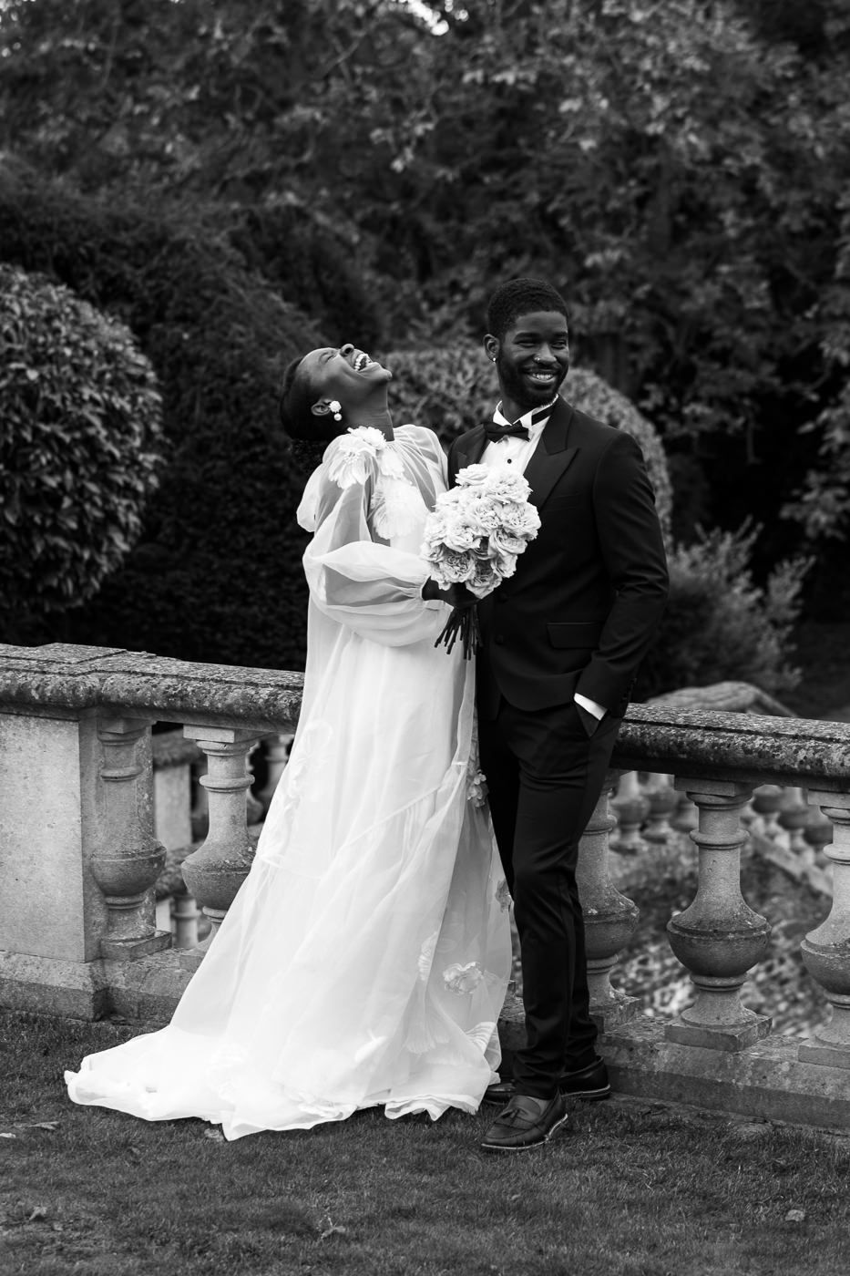 A joyful black and white wedding photo of a couple captured in a garden with stone balustrades and greenery. Euridge Manor Photographer.