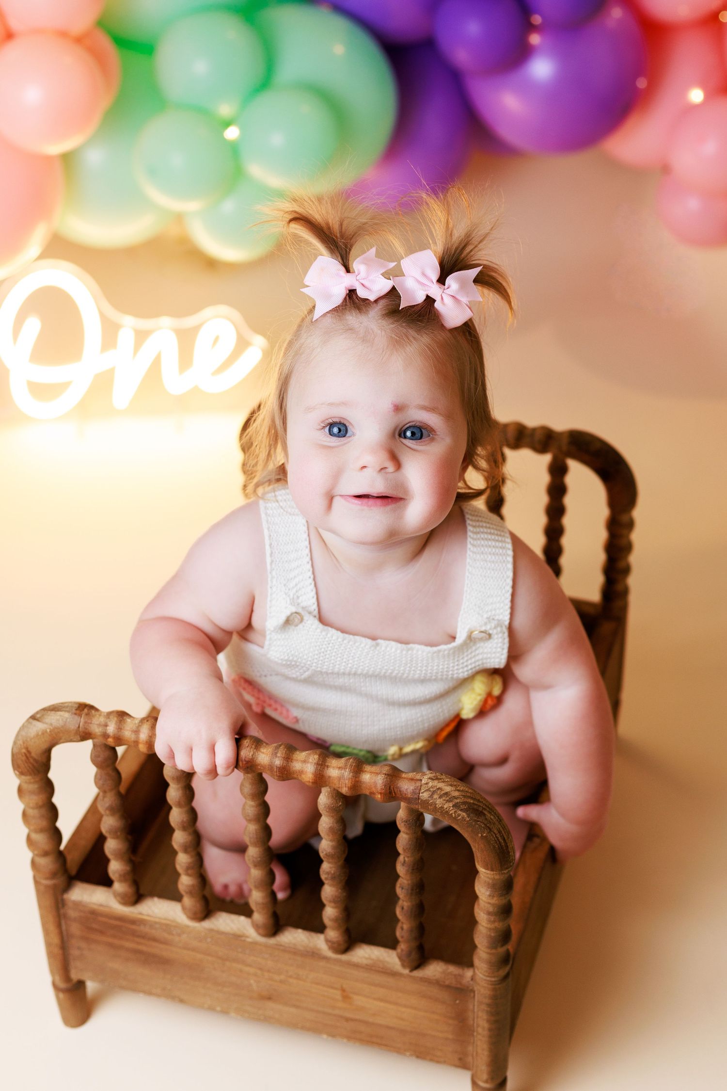 Baby girl with pigtails and pink bows sitting on a little bed surrounded with balloons for a Dalton Georgia Cake Smash