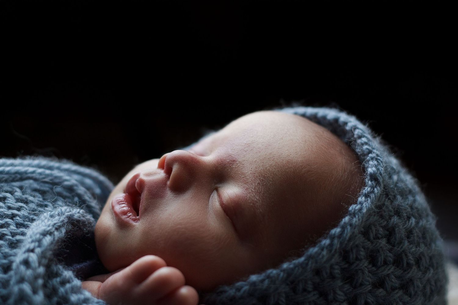 Close-up of a newborn baby boy sleeping peacefully in a chunky sky blue knit wrap.