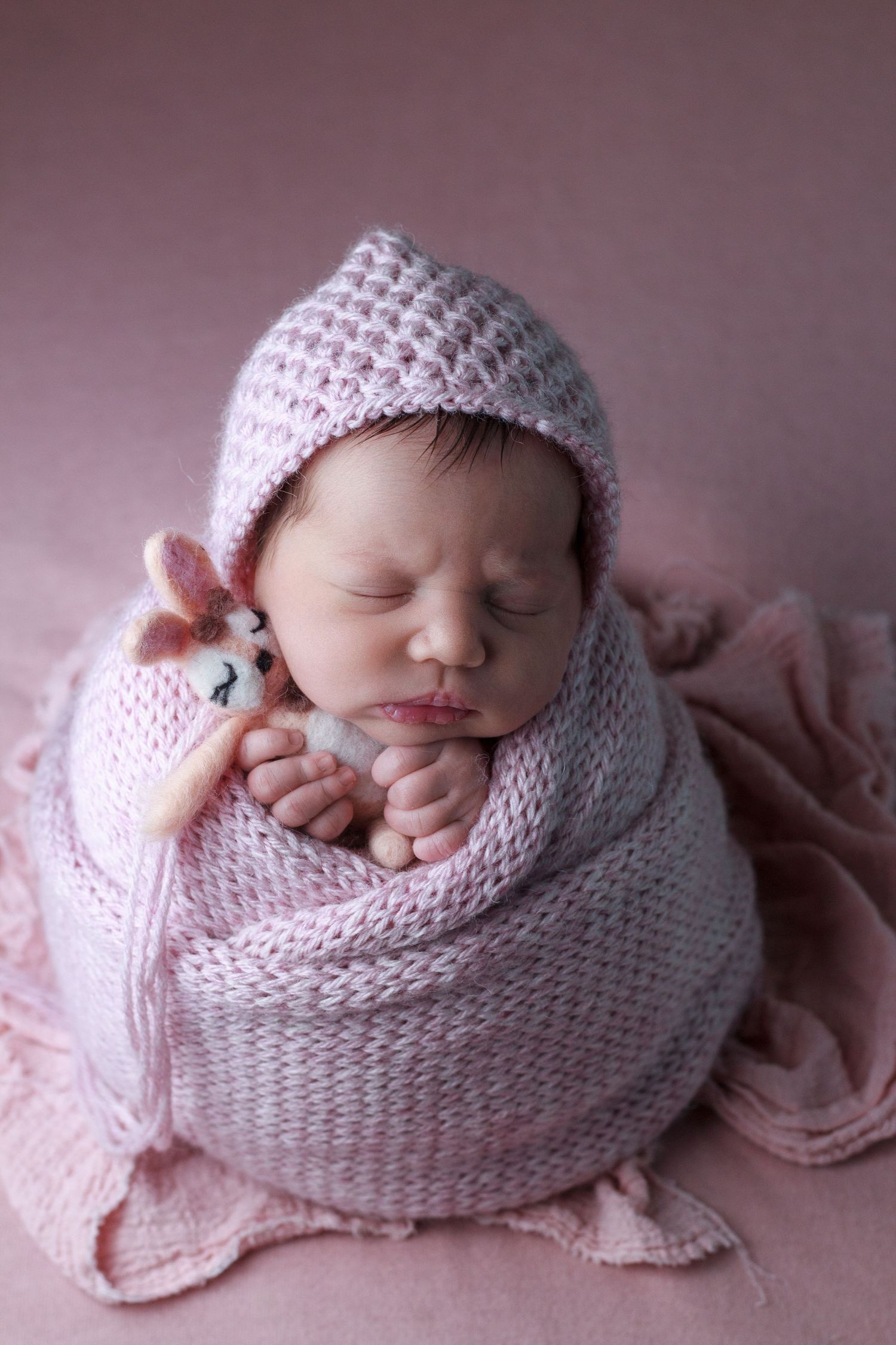 Sweet newborn girl posed on soft pink backdrop in soft pink knit set at in home newborn session