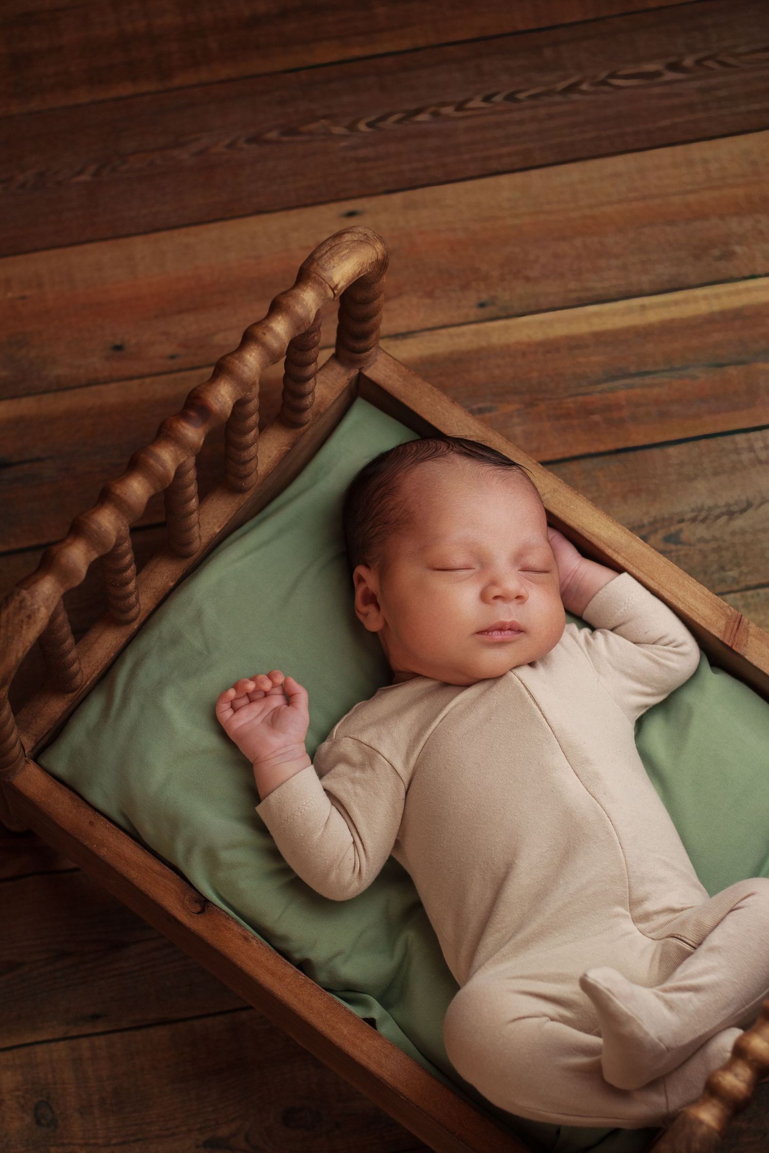 Newborn baby boy sleeping on a tiny wooden spindle bed during his newborn session