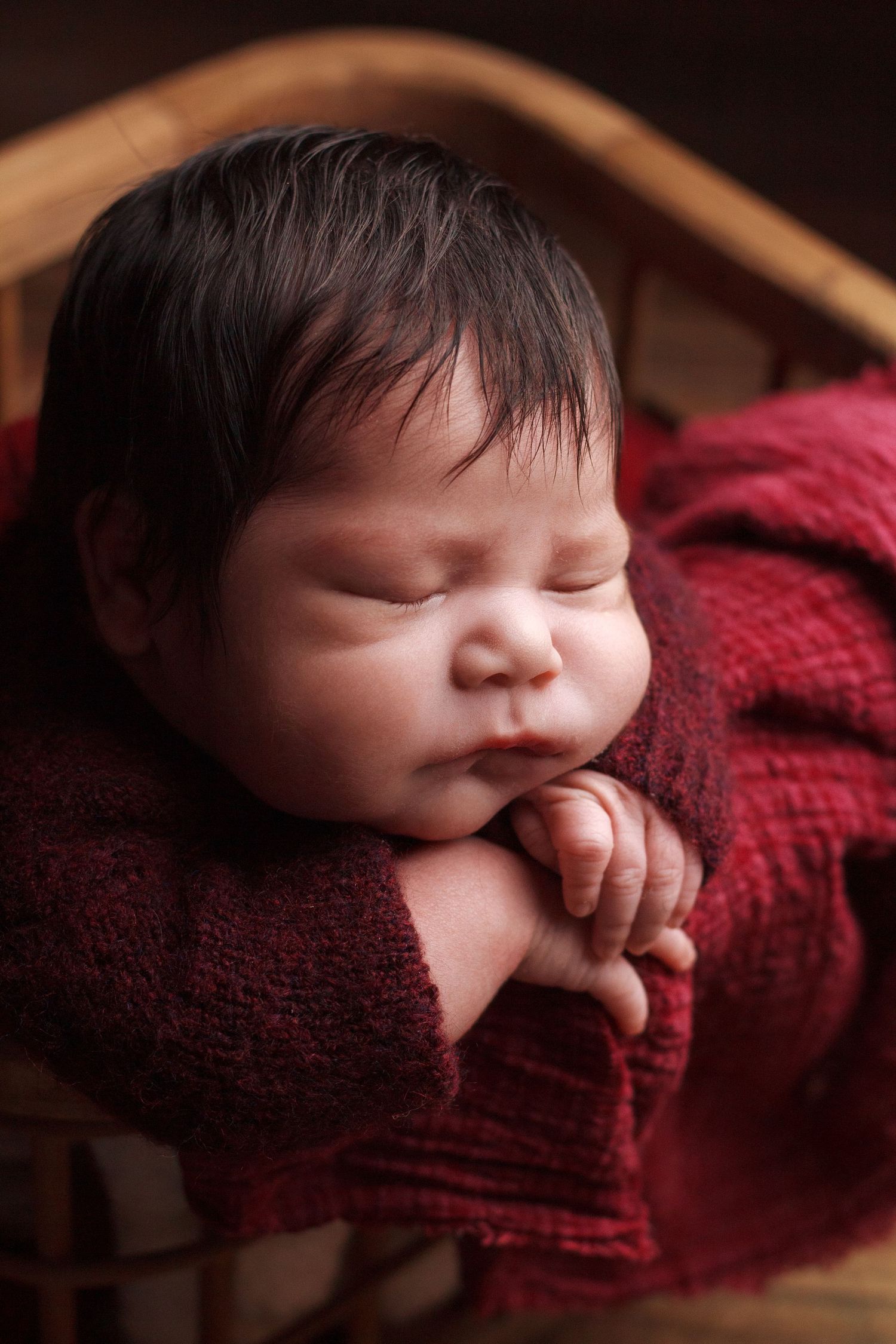 In-home newborn photography session in Dalton GA, baby resting on hands on red fabric in wooden box.