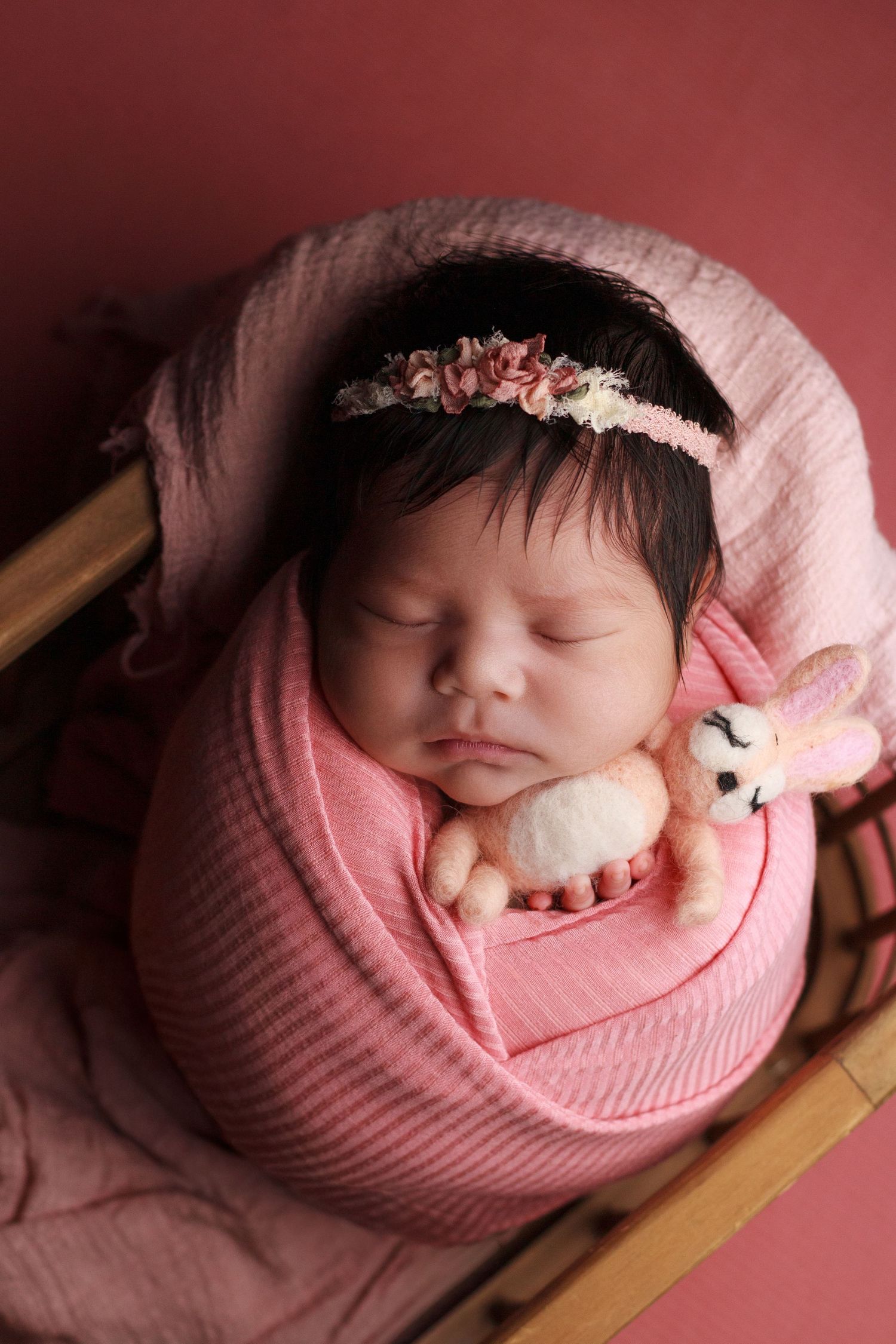 Baby girl wrapped in pink wrap with a pink floral headband in a basket asleep during her in home newborn session in Dalton Georgia