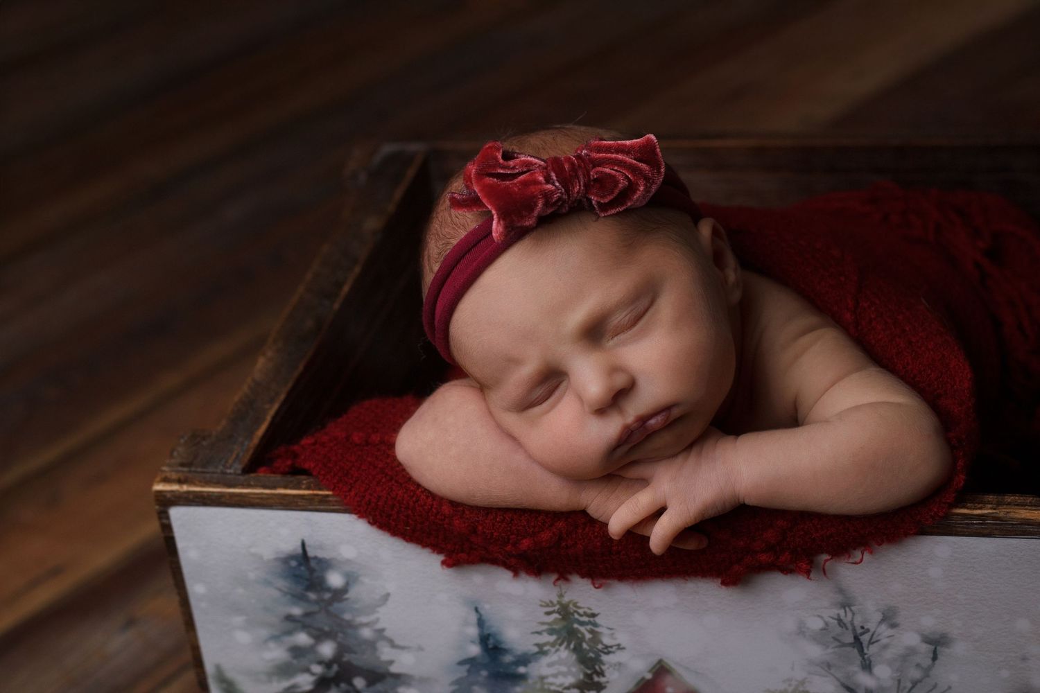 Newborn baby girl wrapped in deep red knit resting in a wooden crate during a newborn photography session in Dalton, Georgia.