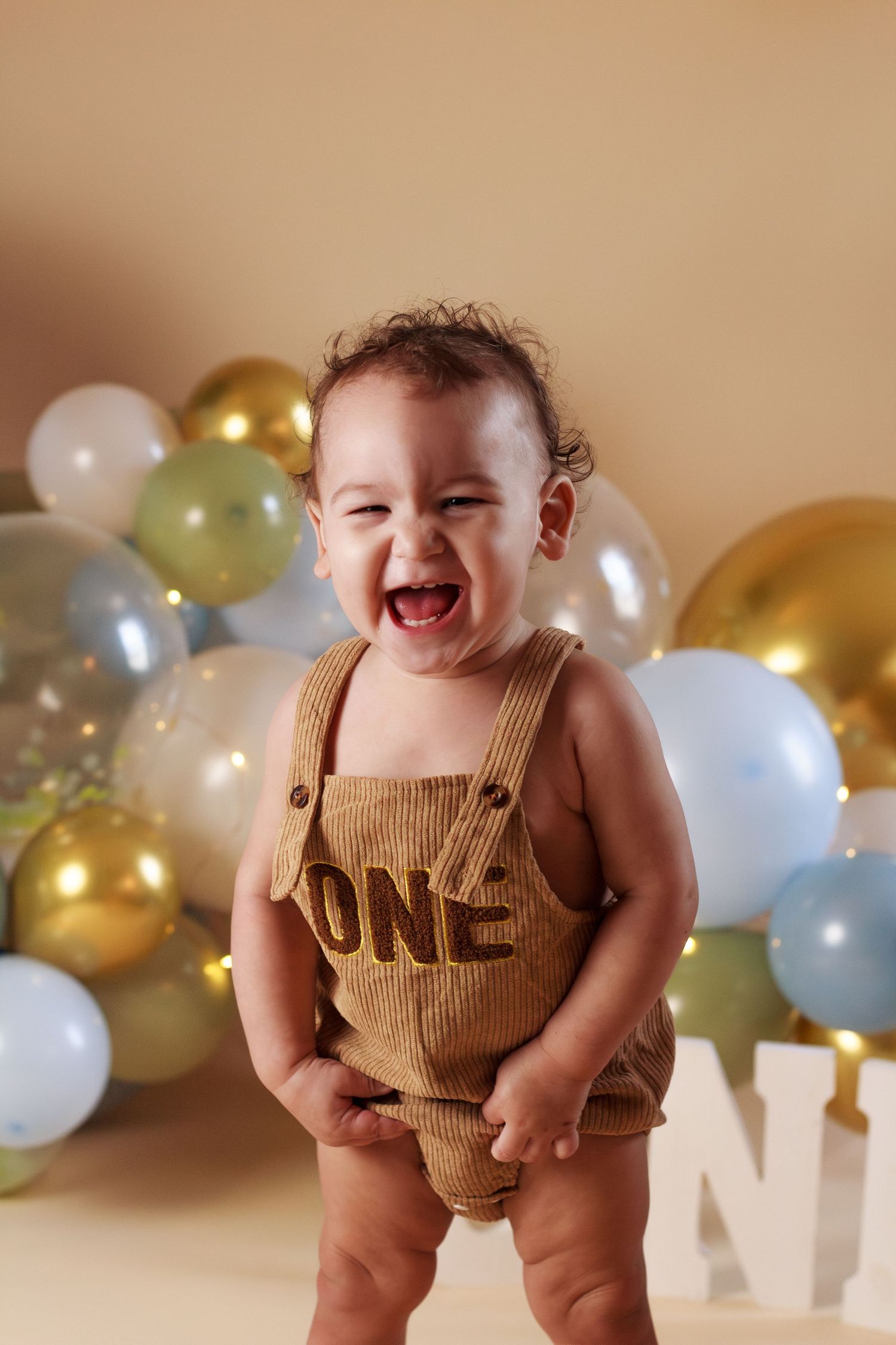 Toddler boy surrounded by blue, green and gold balloons laughing during his cake smash session in Dalton Georgia
