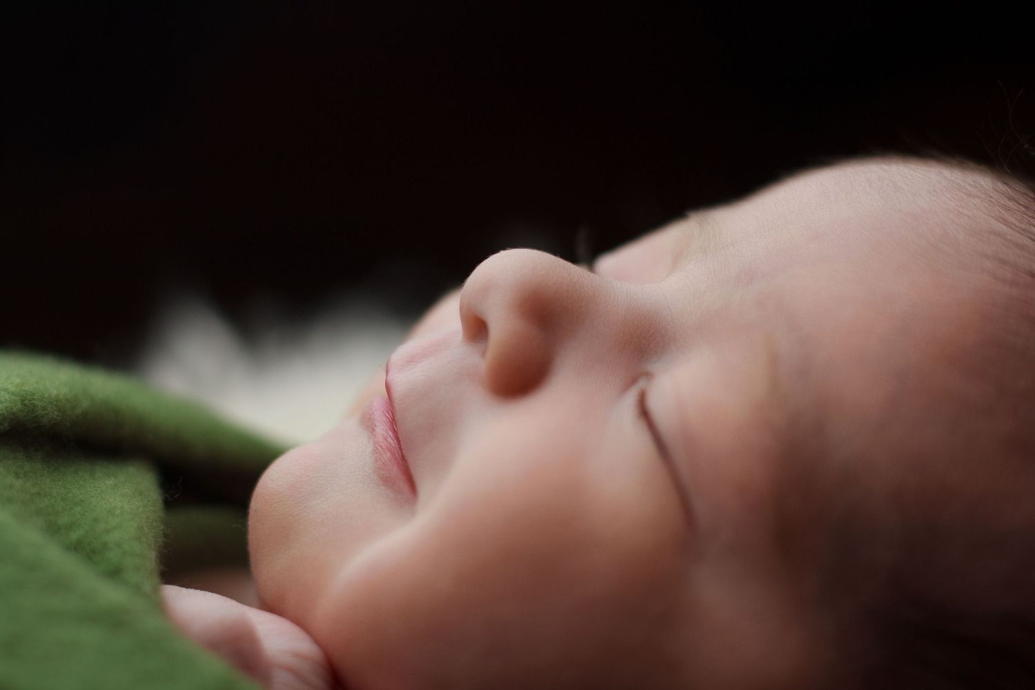 Close-up of a newborn baby sleeping peacefully while wrapped in soft green fabric.