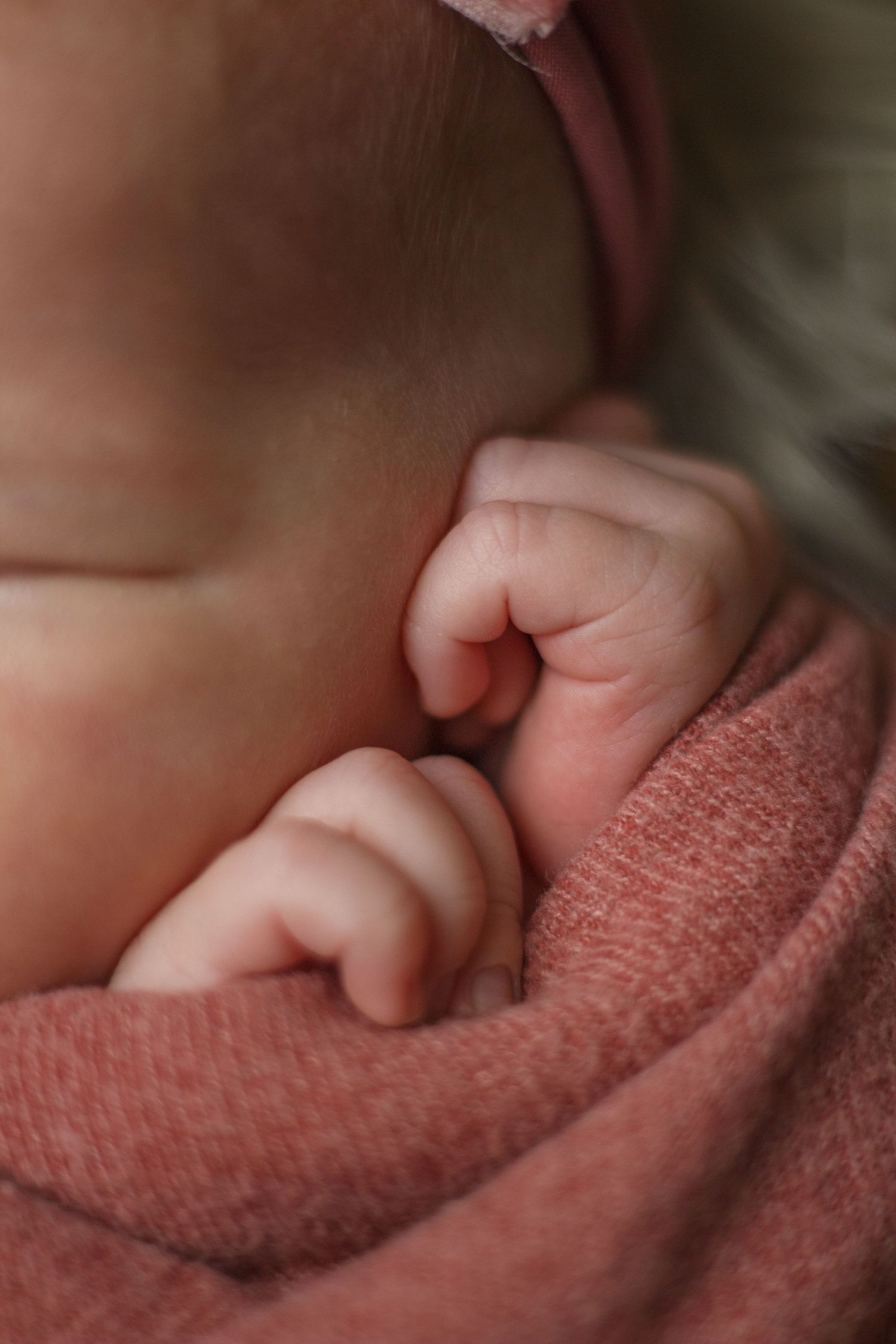 Close-up of newborn wrapped in mauve, closeup hand details.