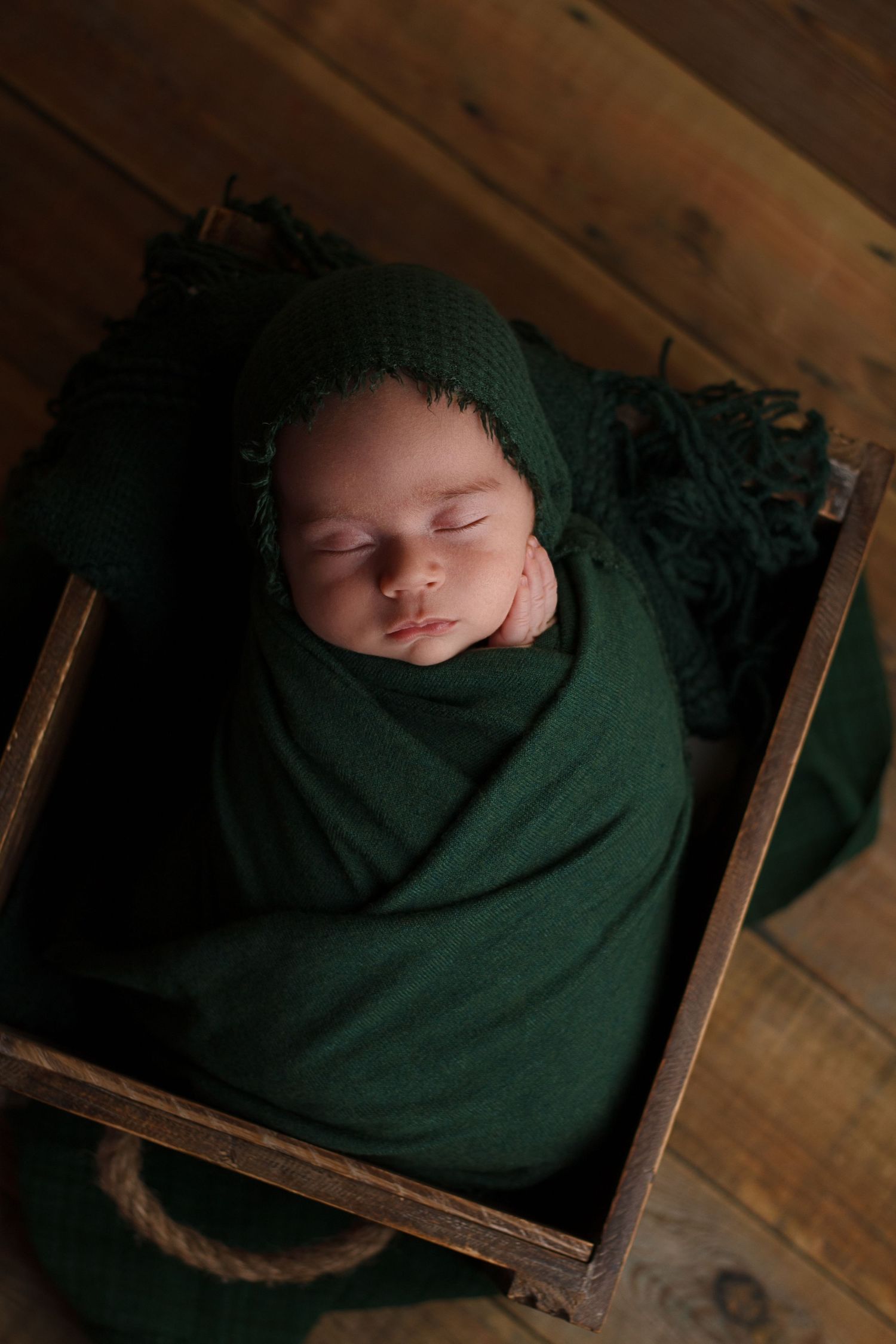Sleeping newborn wrapped in deep green fabric resting in a wooden prop during a studio newborn photography session in Dalton, Georgia.