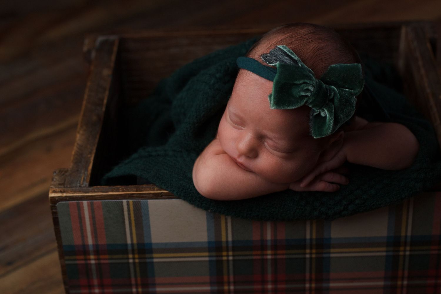 Newborn baby girl wrapped in deep green fabric resting in a wooden crate during a newborn photography session in Dalton, Georgia.