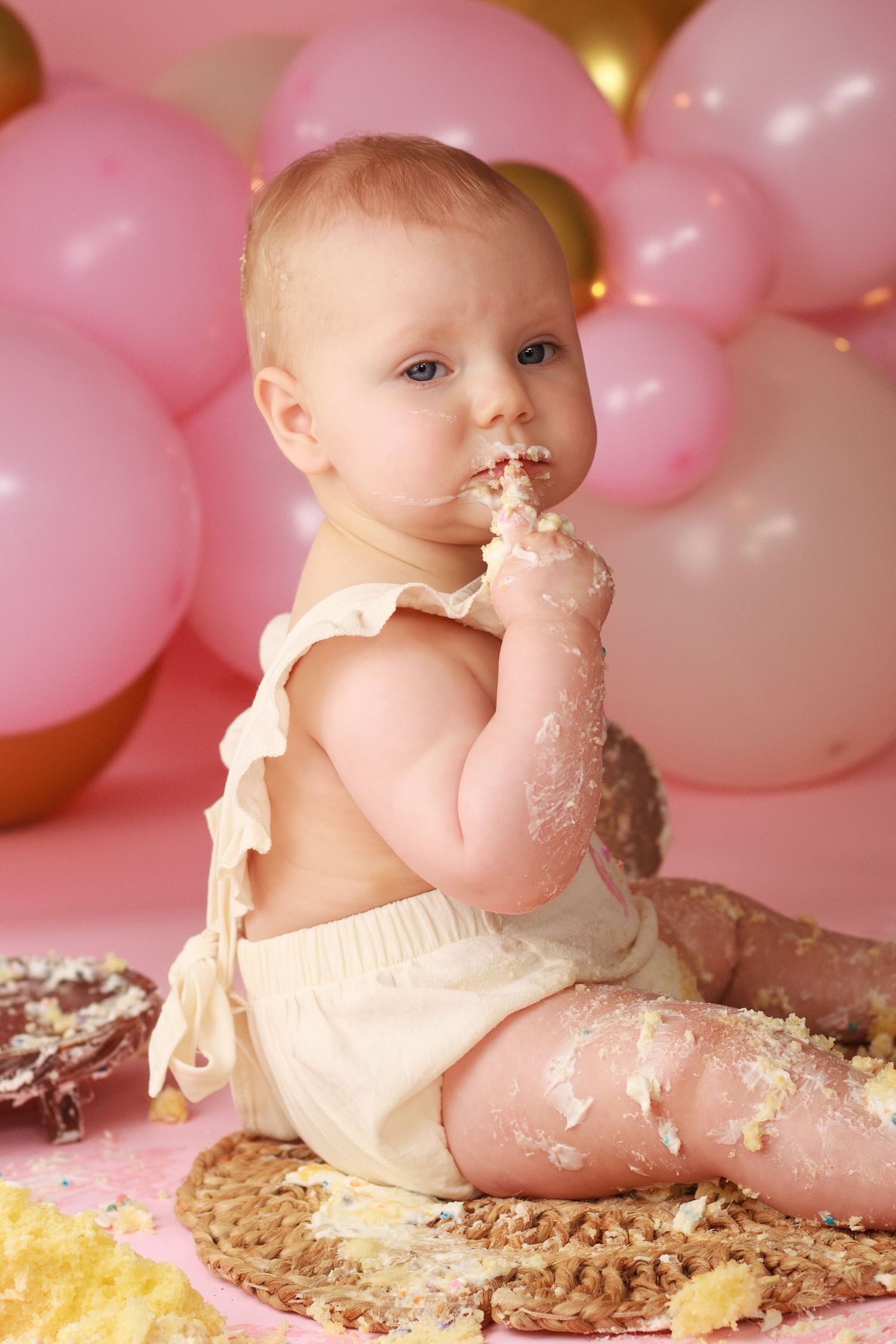 One year old cake smash with frosting covered hands with pink and gold balloon background during a Dalton Georgia Cake Smash Session