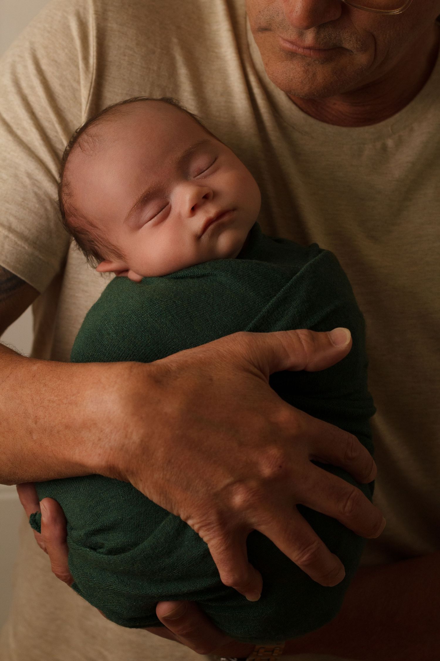 Grandpa gently holding a newborn baby wrapped in green fabric during a newborn photography session in Dalton, Georgia.
