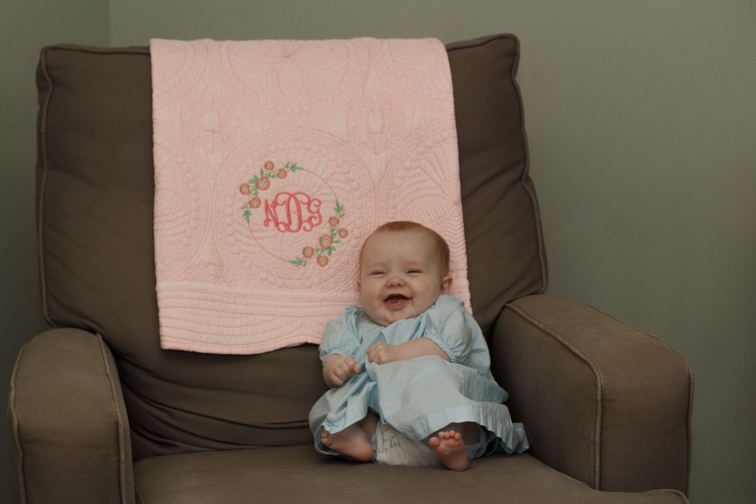 Baby girl sitting in a brown rocking chair featuring a monogramed blanket of her initials during an in home family session in Dalton Georgia