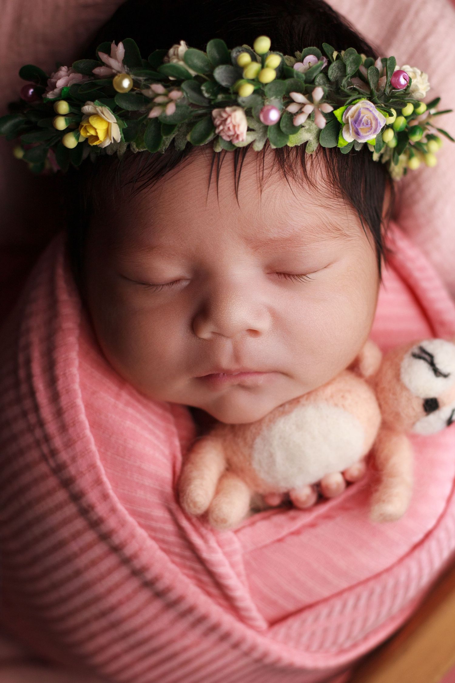Newborn baby girl wrapped in soft pink fabric wearing a delicate floral crown during a newborn photography session in Dalton, Georgia.