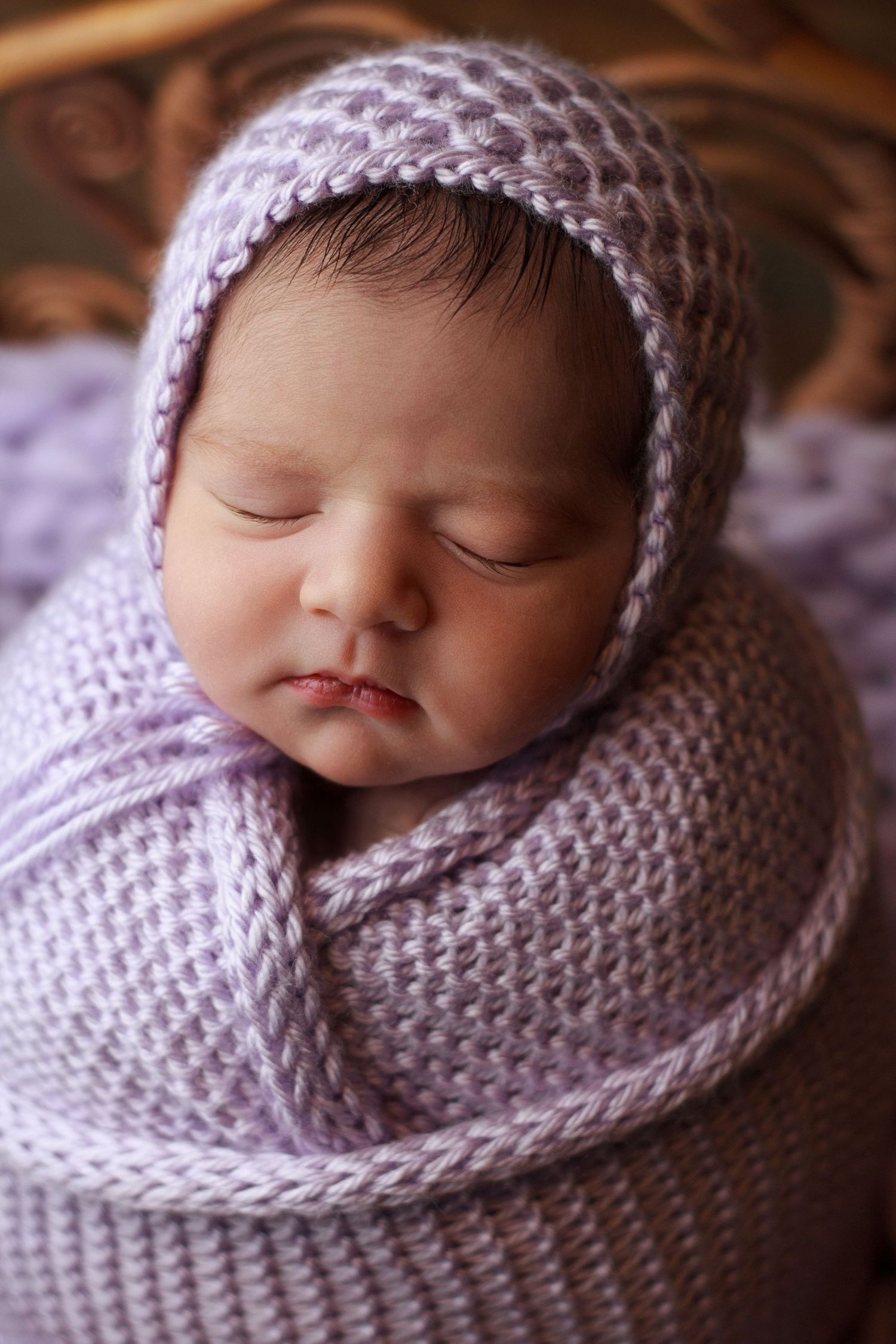 Newborn baby wrapped snugly in a soft lavender knit wrap during a newborn session.
