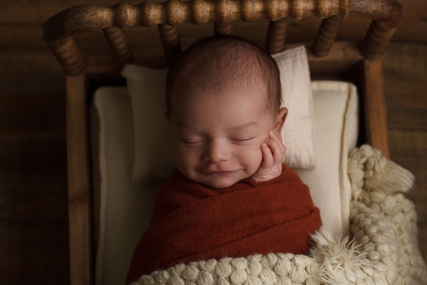 Newborn baby sleeping in a small wooden bed wrapped in rust-colored fabric during a newborn photography session in Dalton, Georgia.