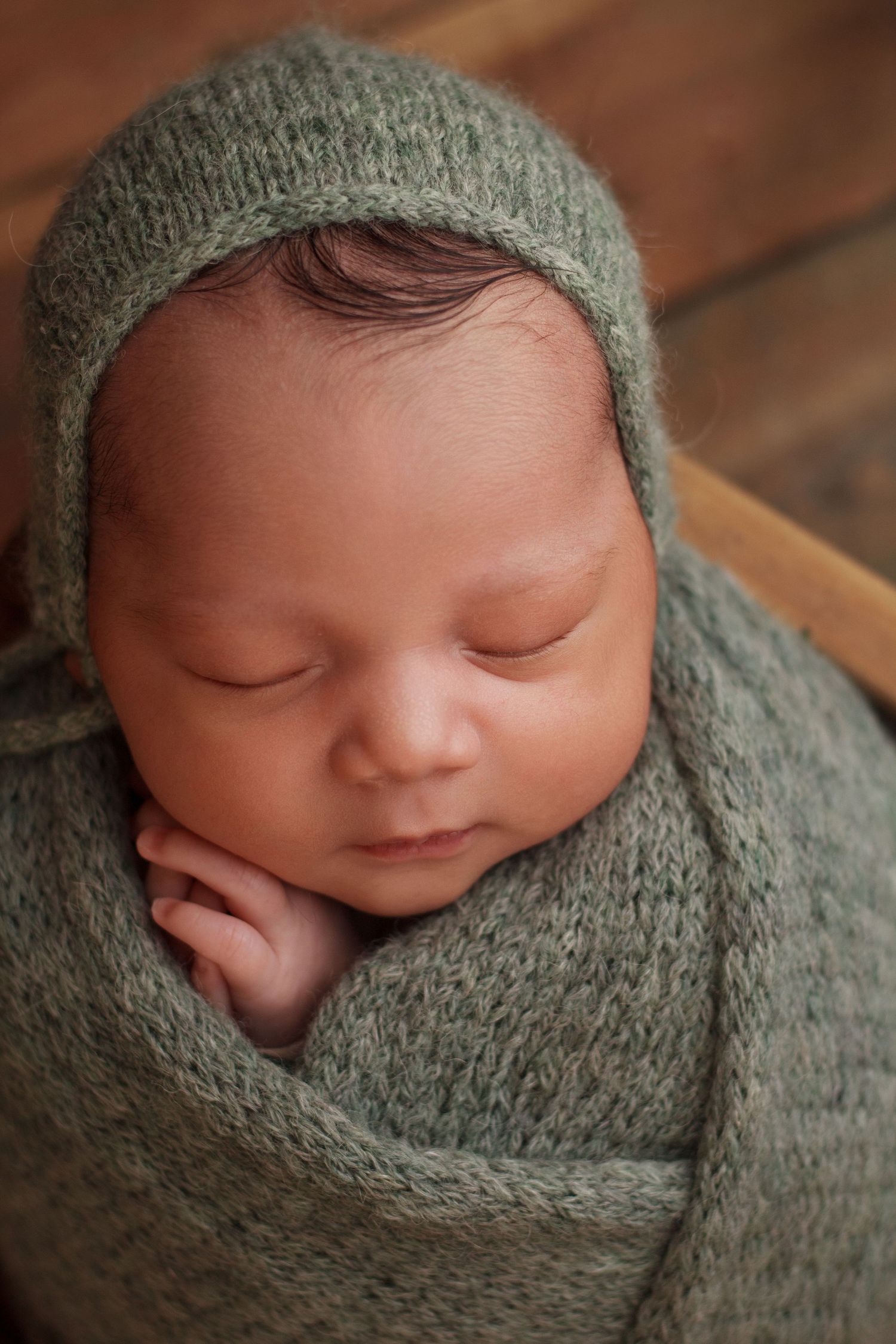 Newborn baby boy wrapped in sage green wrap and matching bonnet sleeps peacefully in a wooden crate during a Riggold Georgia Newborn session