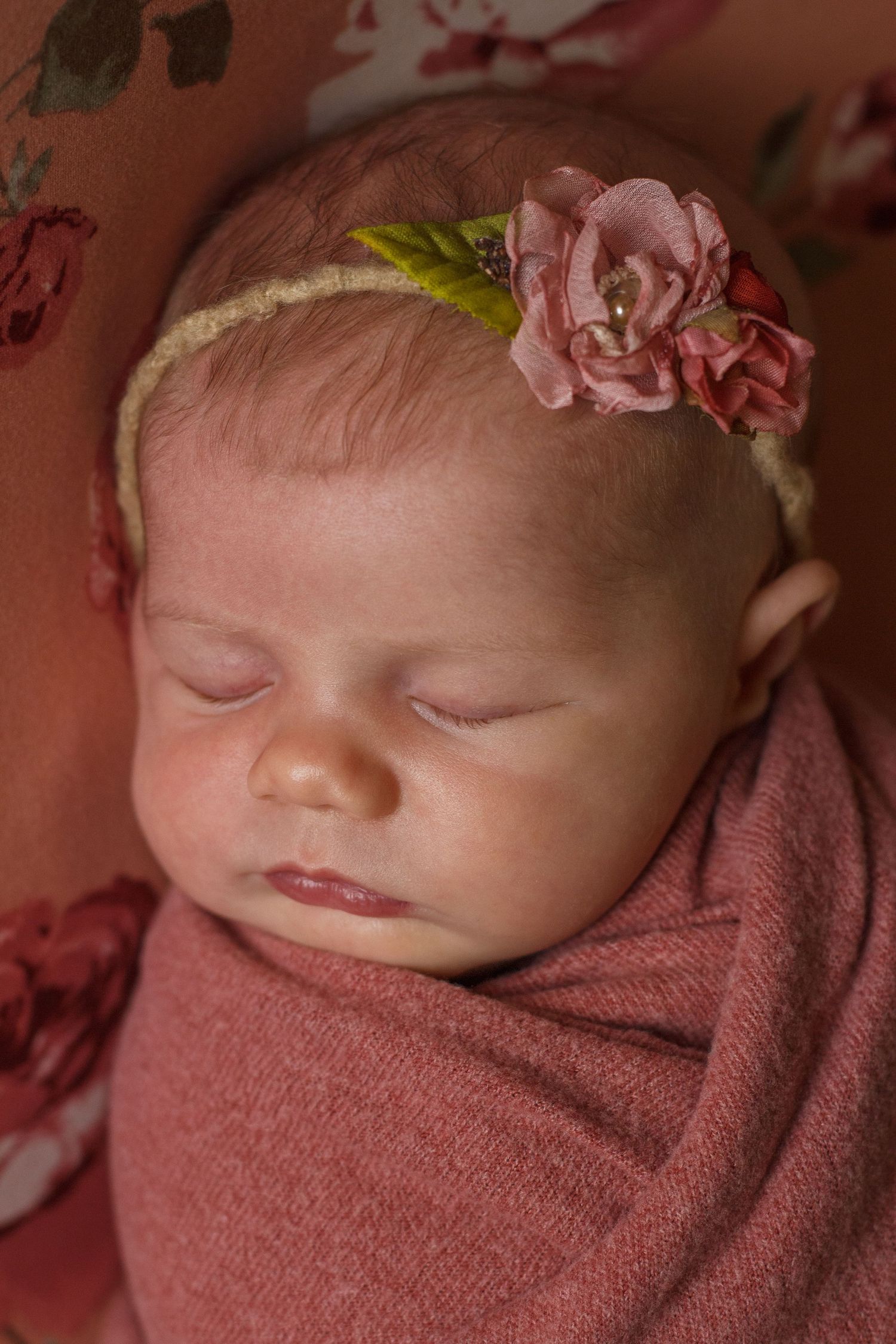 Newborn girl in soft mauve wrap, posed with chin on hands