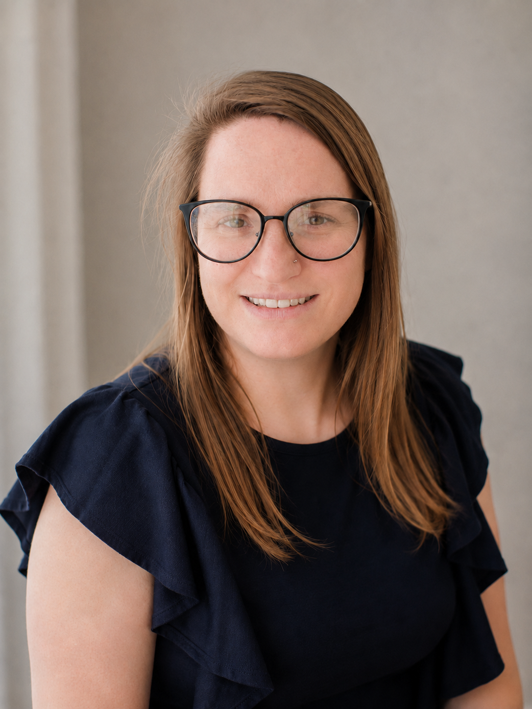 Professional portrait of photographer Tiffany Vick of drifting Feathers Photography with brown hair and glasses wearing a navy blue top.