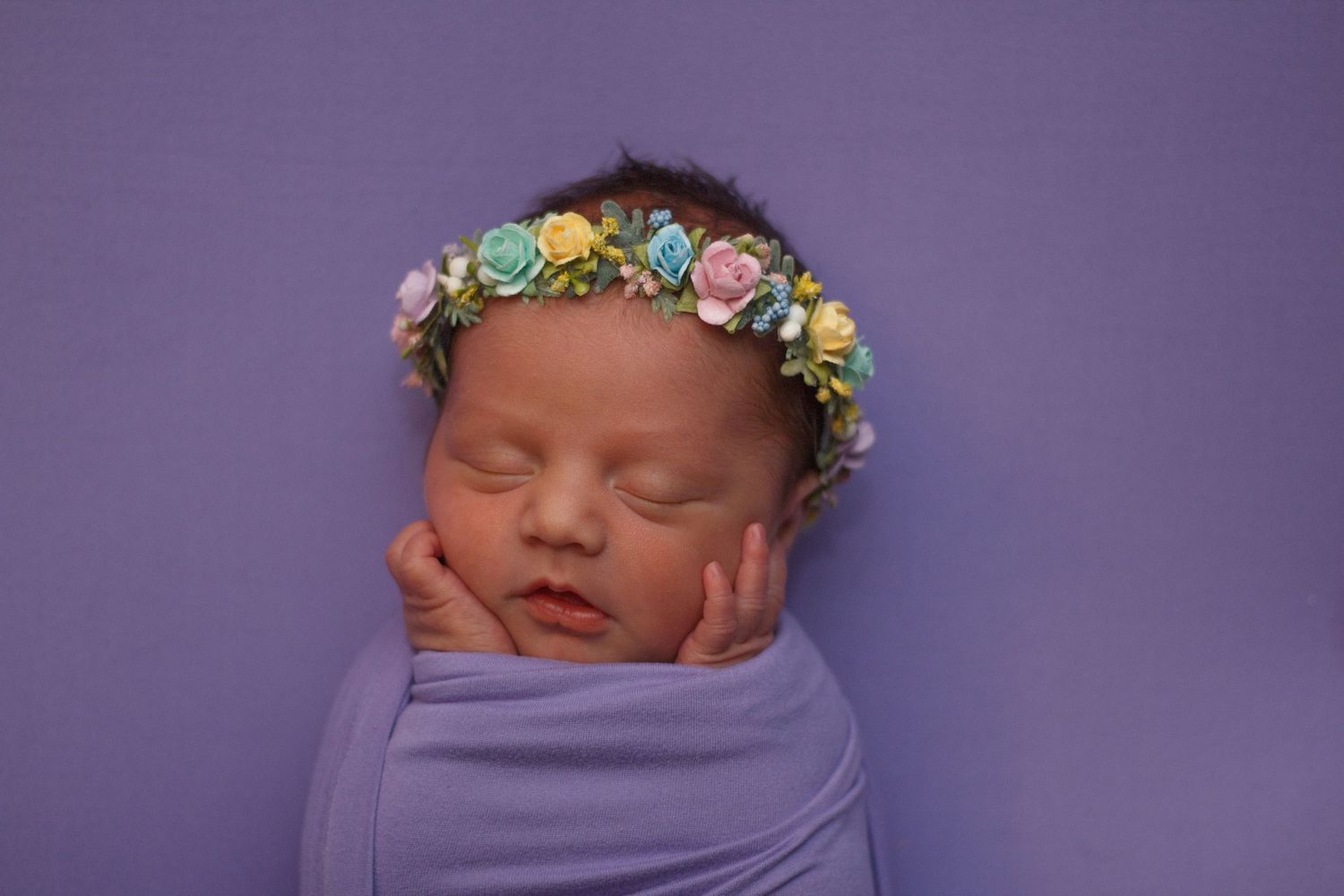 Newborn baby girl swaddled in purple wrap with floral headband, posed on violet backdrop – Chatsworth newborn photography