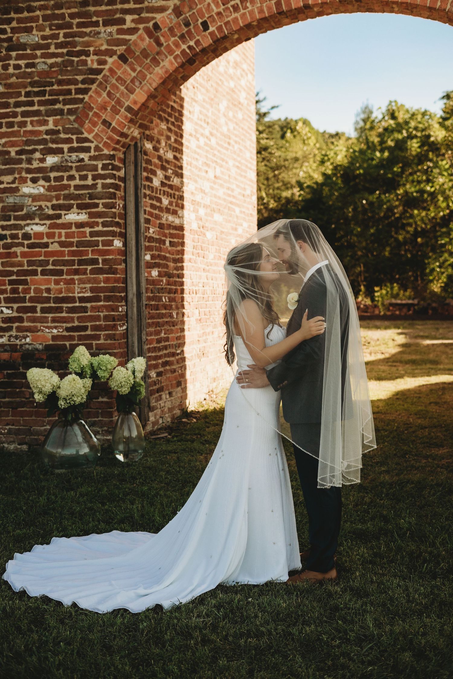 Romantic wedding couple portraits against a brick wall exterior in natural sunlight.