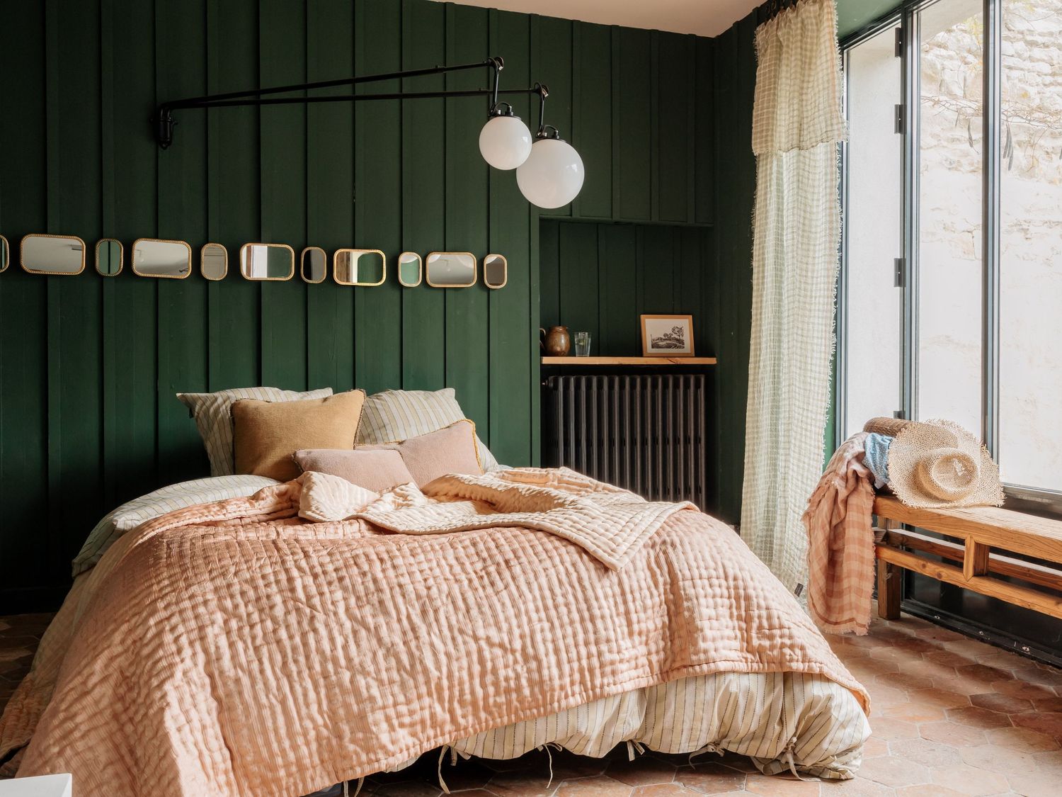 A modern bedroom features dark green walls contrasting with soft pink bedding and natural light from large windows.