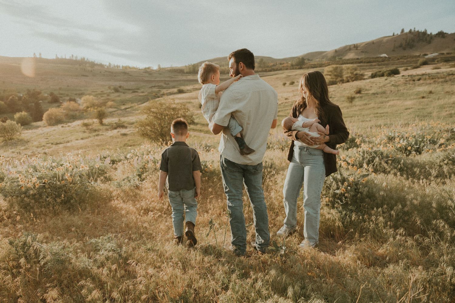 Family standing together in grassy field at sunset with blue sky for family photos in Coldstream bc
