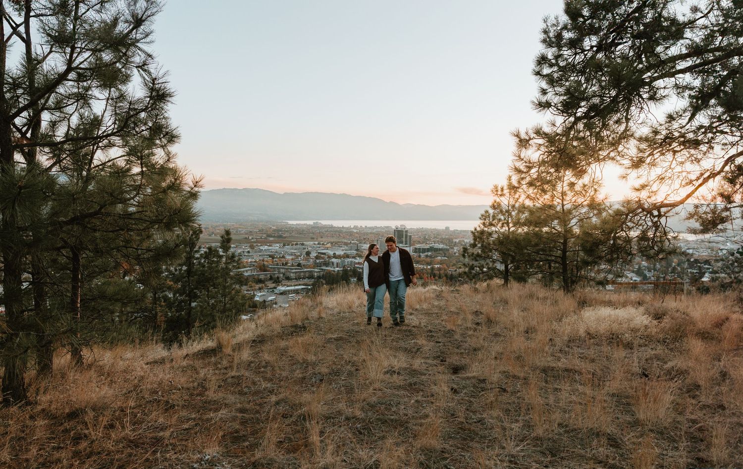 couple walking together in grassy field with large trees in kelowna bc during couples session