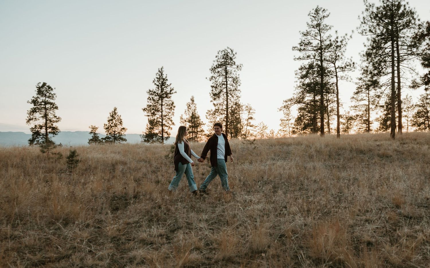 kelowna bc couples session with couple walking hand in hand through tall grass at golden hour in kelowna bc
