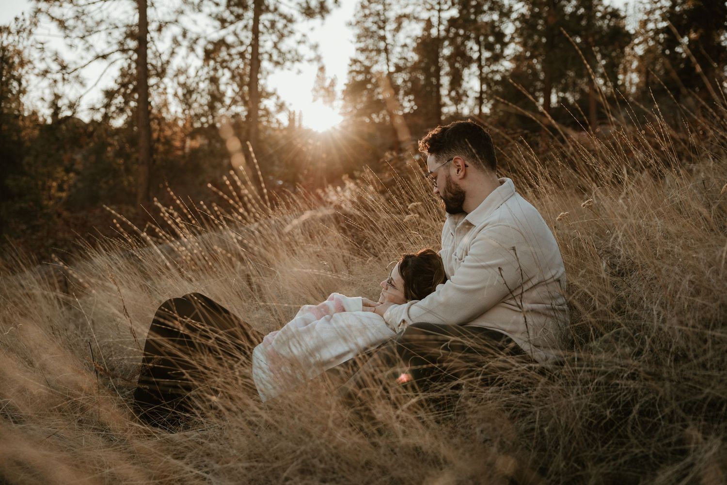 candid moment of couple laying together in tall yellow grass during engagement session in kelowna bc