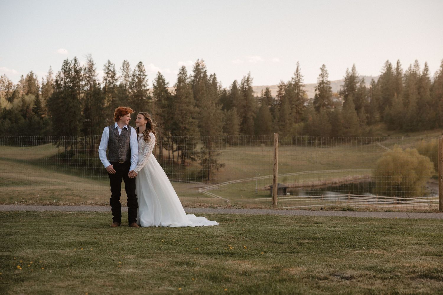 bride and groom standing together looking at each other on their farm in spalumcheen bc at sunset