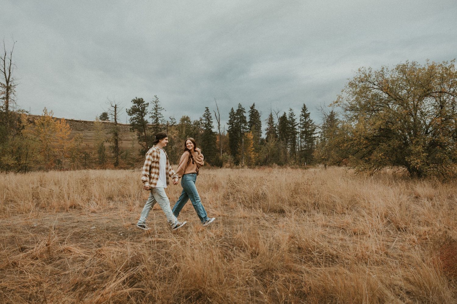 couple laughing together while walking through an open field at sunset in the okanagan