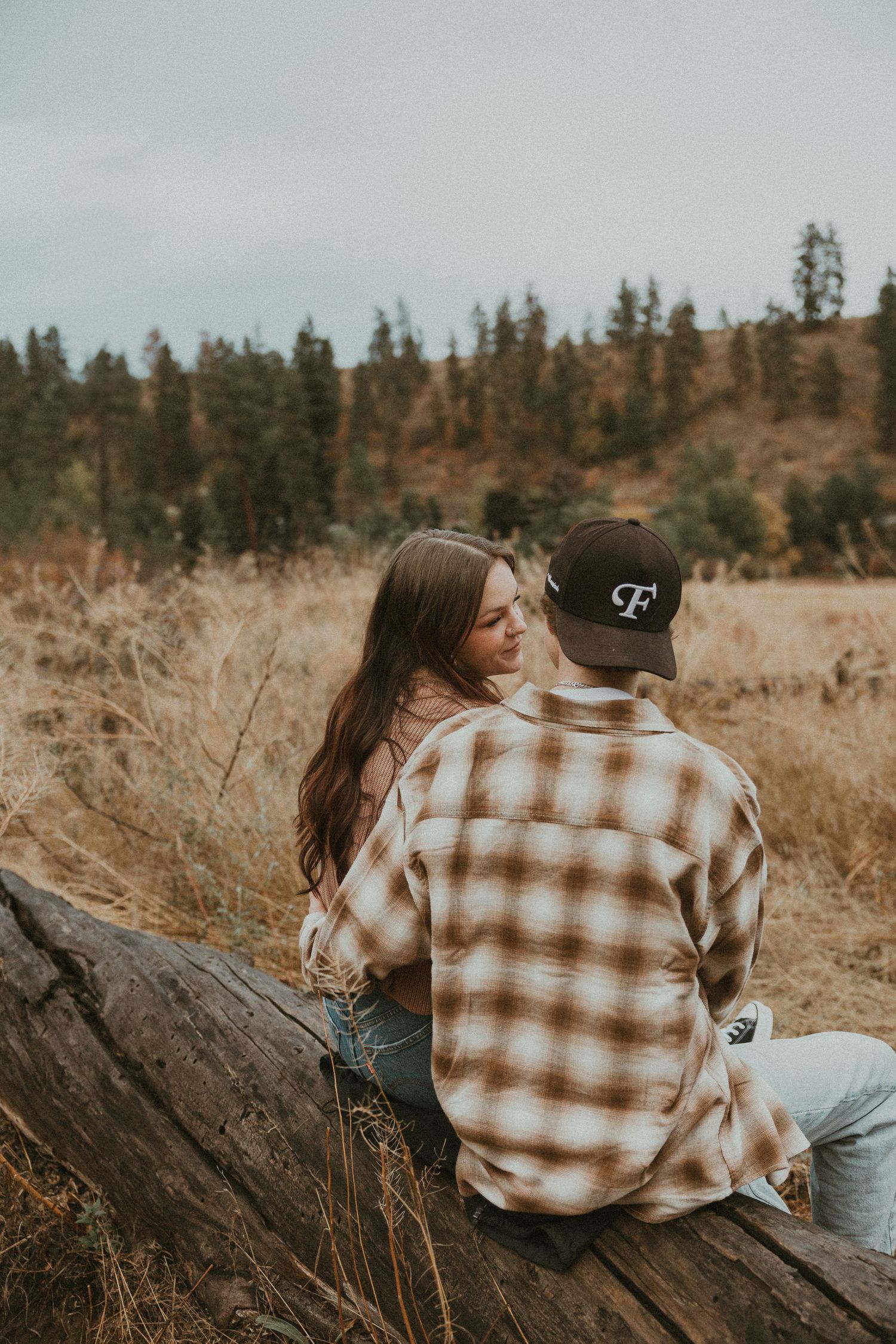 close up detail of couple sitting on a log in a grassy field, capturing relaxed and candid couple moments