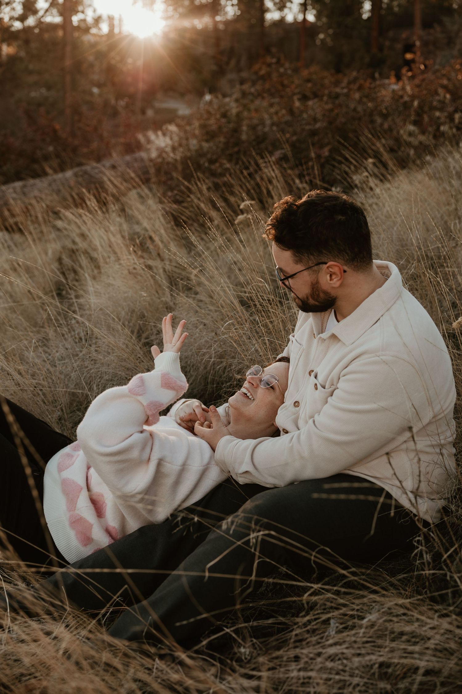 couple excitedly admiring her engagement ring during sunset surrounded by tall yellow grass during engagement session in kelowna bc