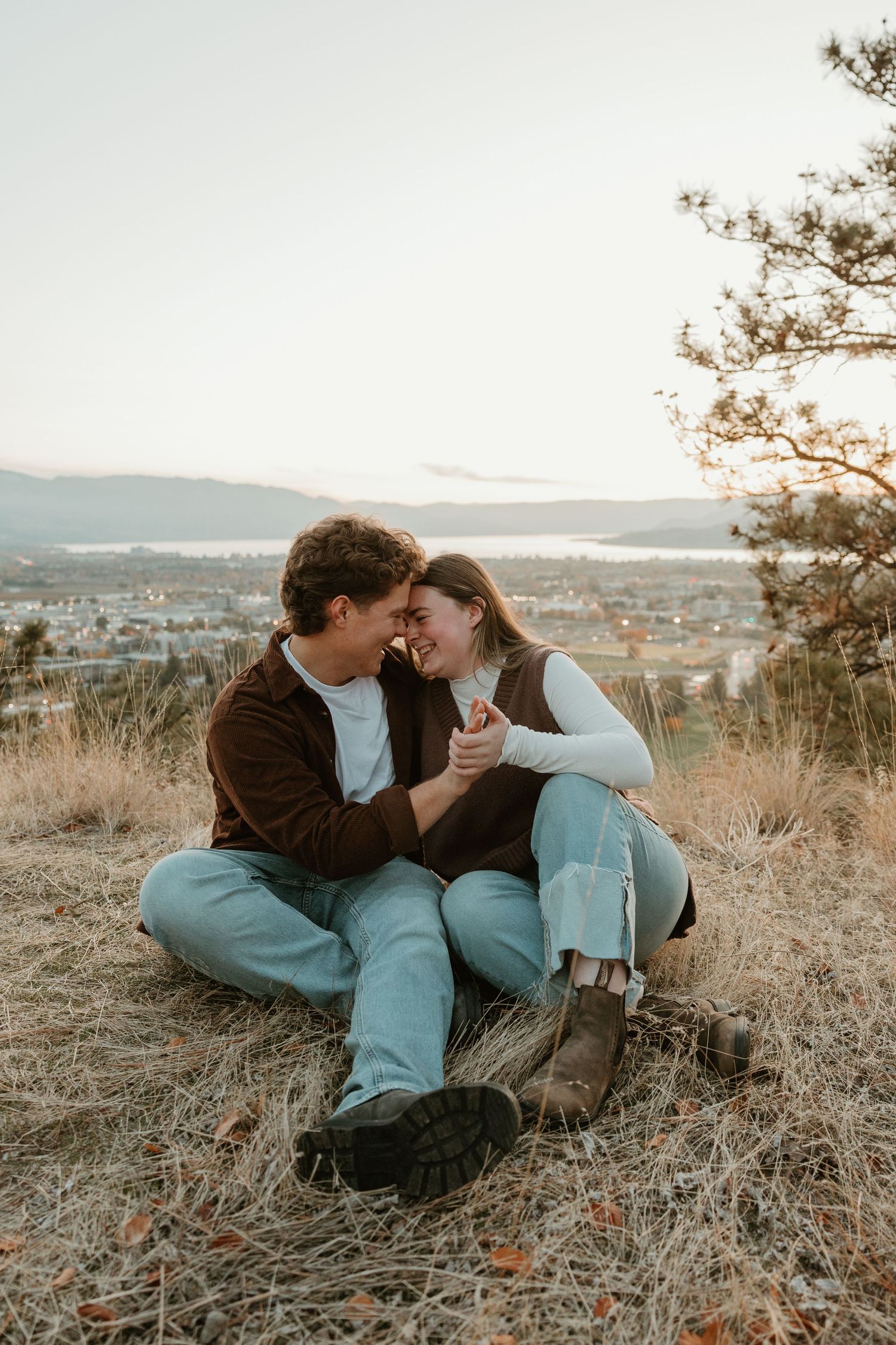 couple snuggling together in grassy field overlooking okanagan lake at sunset