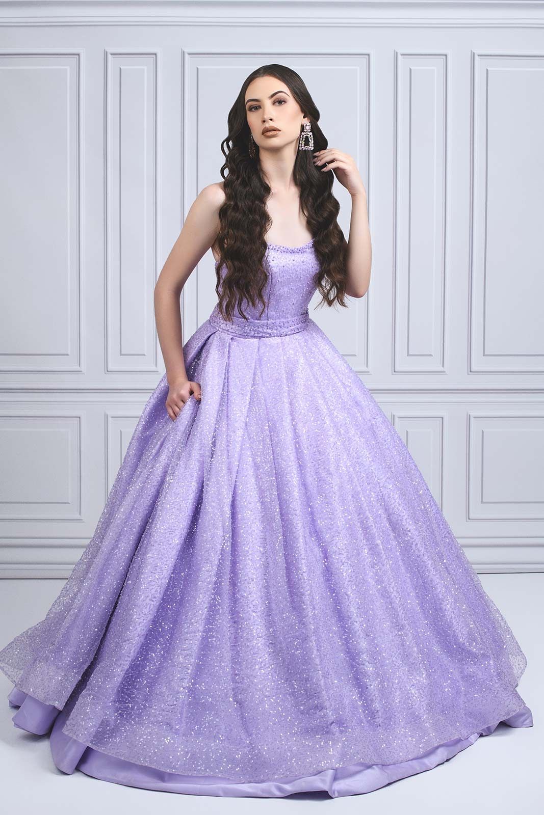 A stunning lilac ball gown with glitter shimmer fabric and strapless bodice against a classic gray paneled wall.