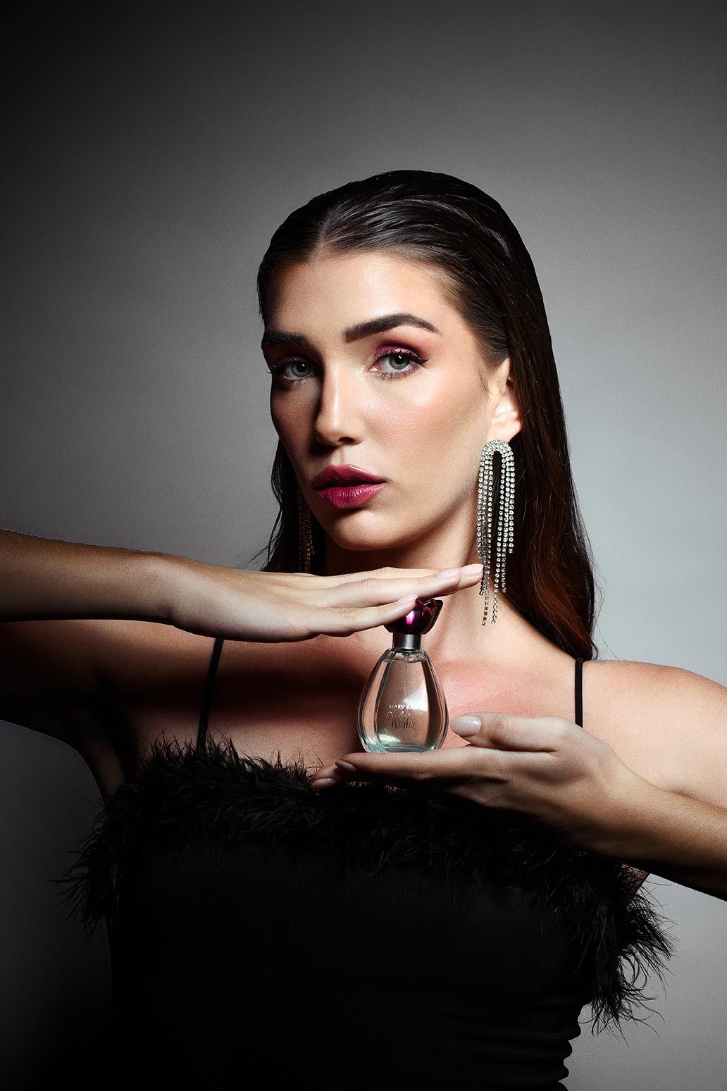 Glamorous fashion portrait showing dramatic lighting, sparkly rhinestone earrings, black feathered top and bold red lipstick.