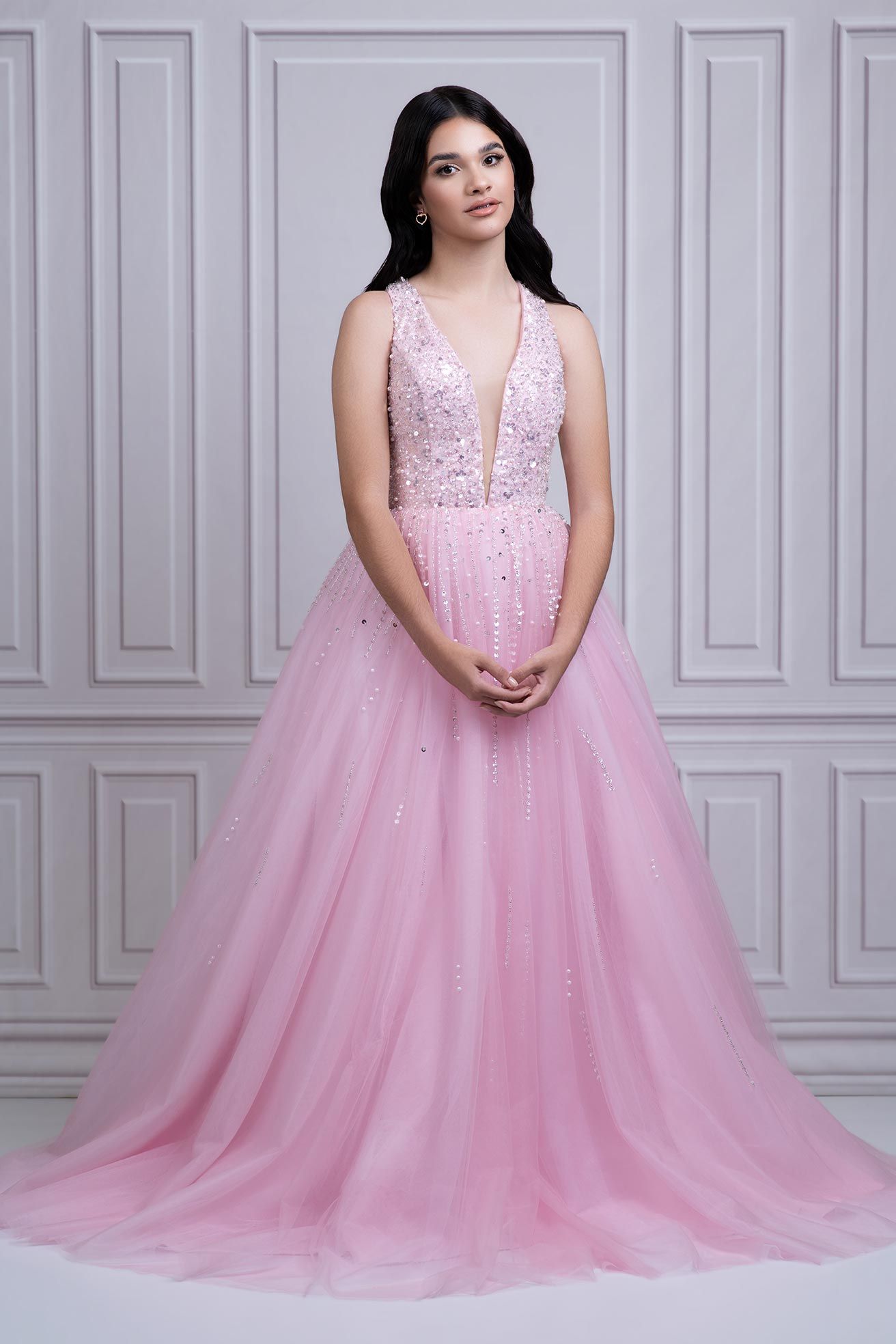 A stunning pink ball gown with a beaded bodice and flowing tulle skirt photographed against a gray paneled wall.