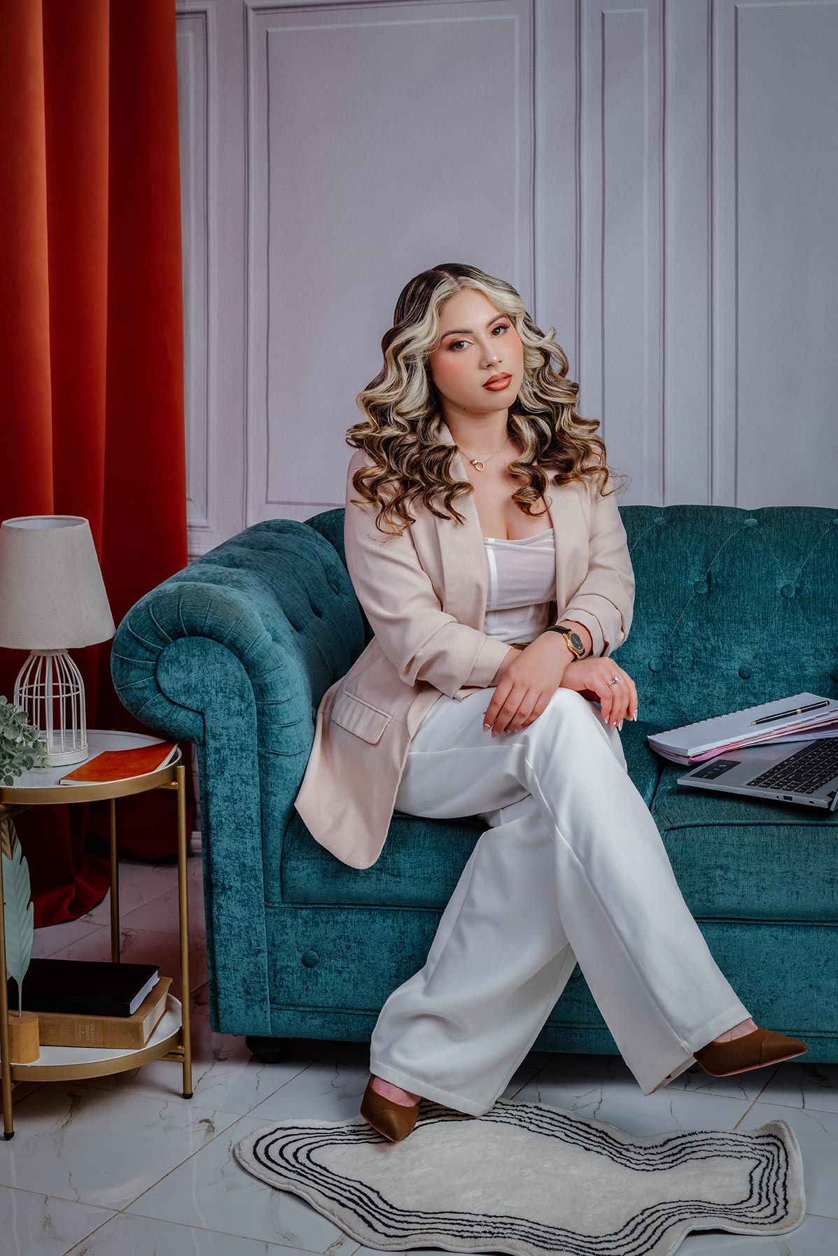 Professional fashion portrait on teal velvet couch with elegant beige blazer and white pants.