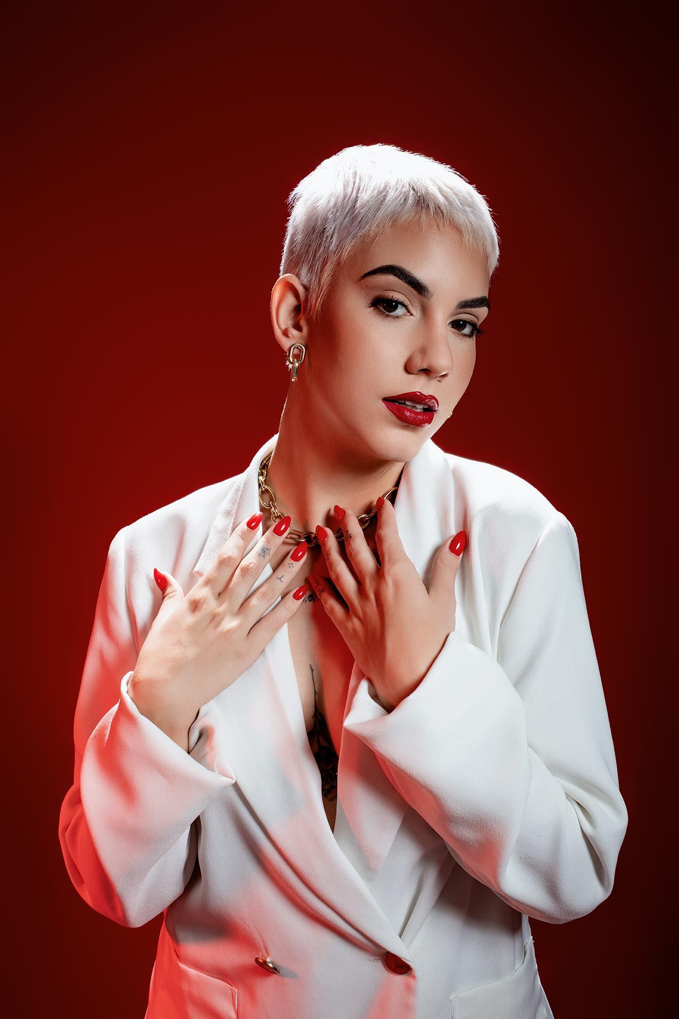 Dramatic studio portrait against red background featuring white blazer and bold red lipstick.