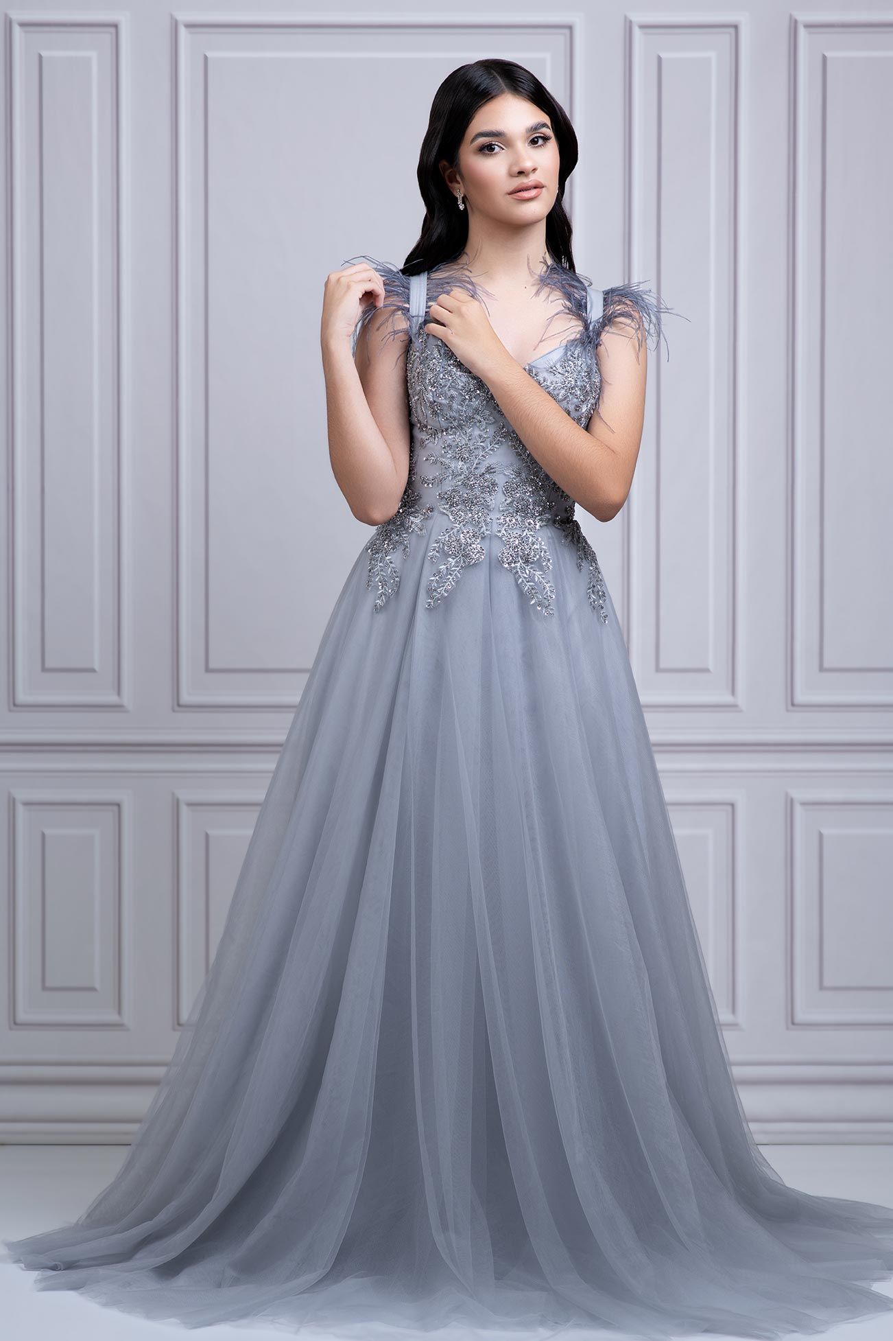 Ethereal silver-grey tulle evening gown with lace applique bodice and sweeping A-line silhouette against white wall.