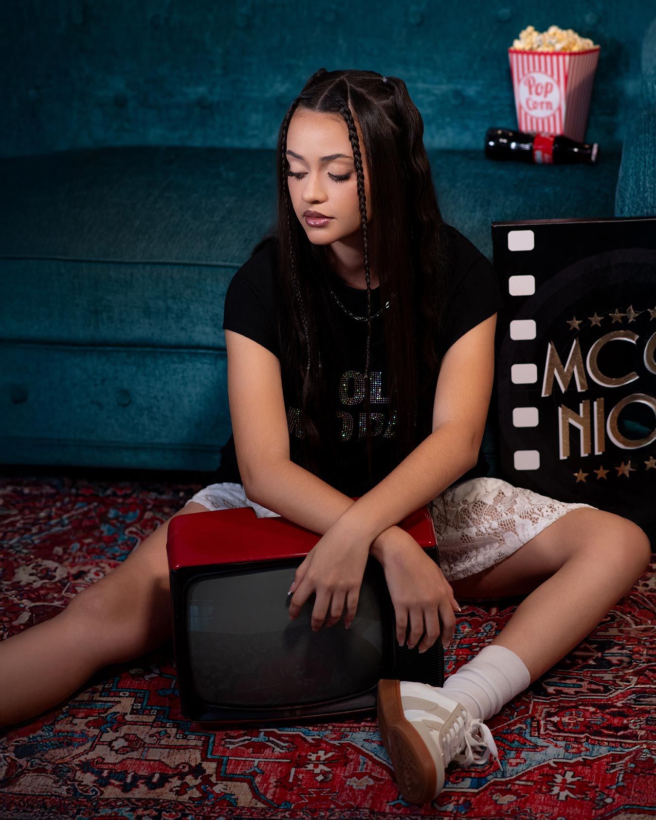 A dark movie night scene with a film strip light box, popcorn and someone sitting on a vintage red carpet.