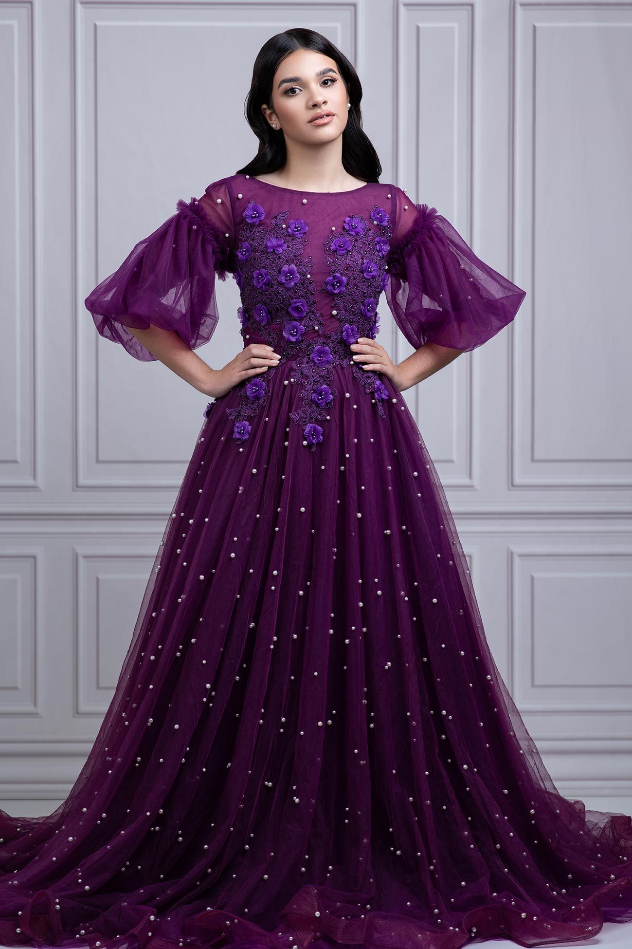 Elegant purple tulle ball gown with puff sleeves, floral appliques and sparkling sequins on a gray backdrop.