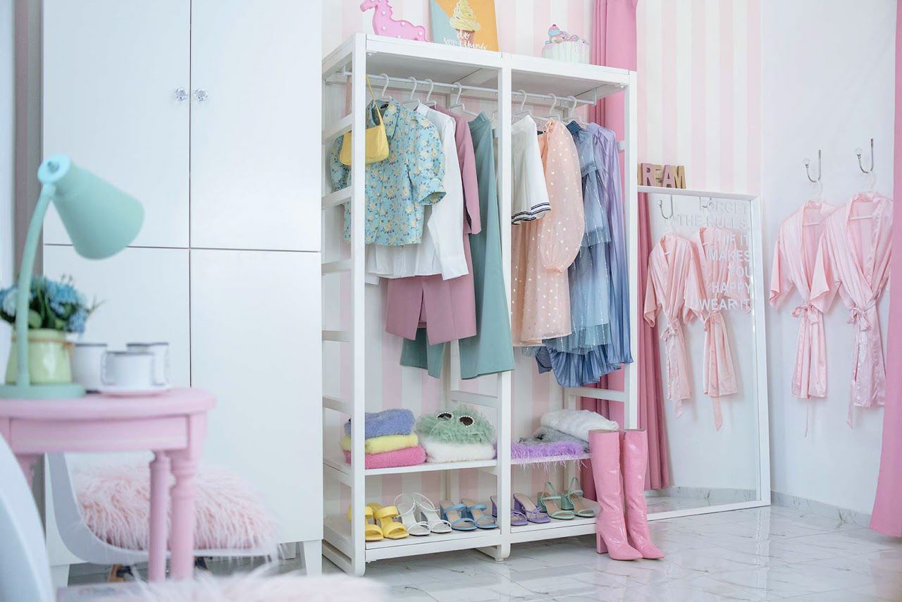 A pastel-colored children's bedroom with an open white wardrobe rack displaying neatly arranged clothing and shoes.
