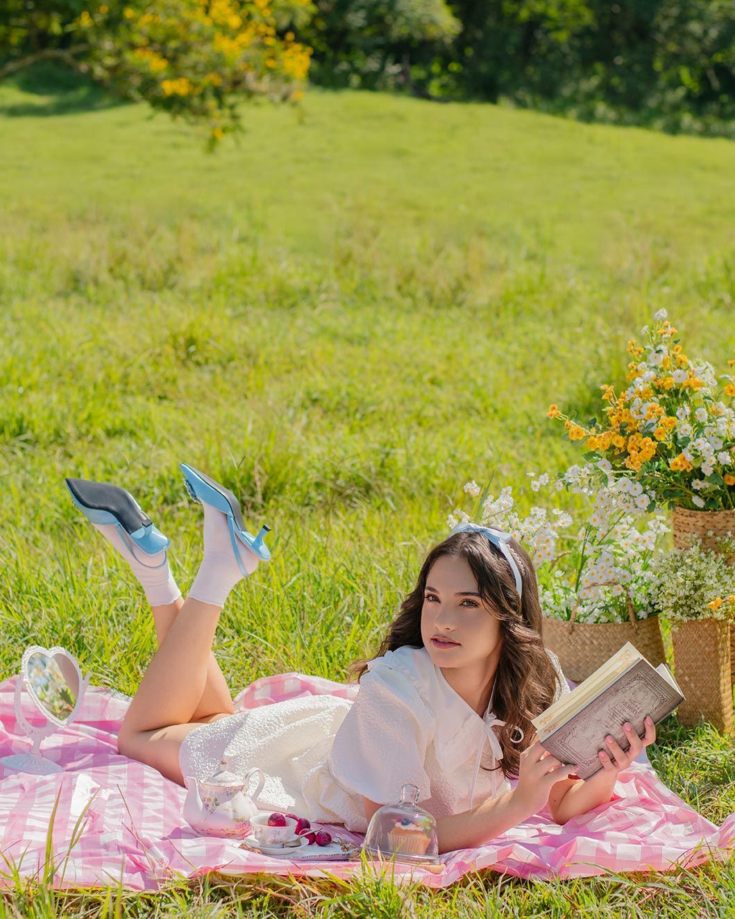 A picturesque summer picnic scene with someone reading on a pink blanket amid flowers and greenery in a sunny meadow.