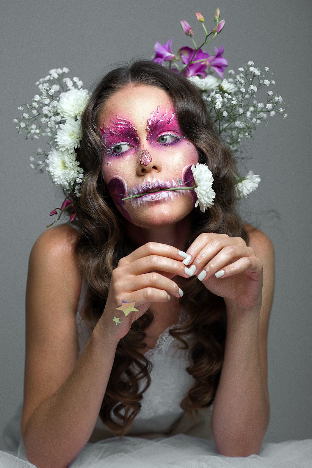 Creative Día de los Muertos sugar skull makeup with pink eyeshadow, white flowers and baby's breath adorning long wavy hair.